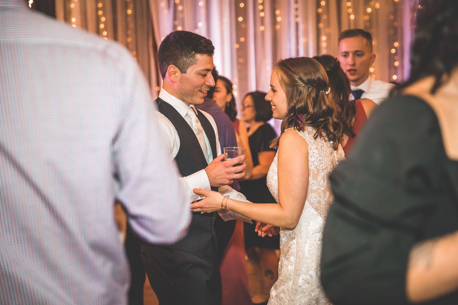 Guests dancing and celebrating at an indoor wedding reception with string lights.