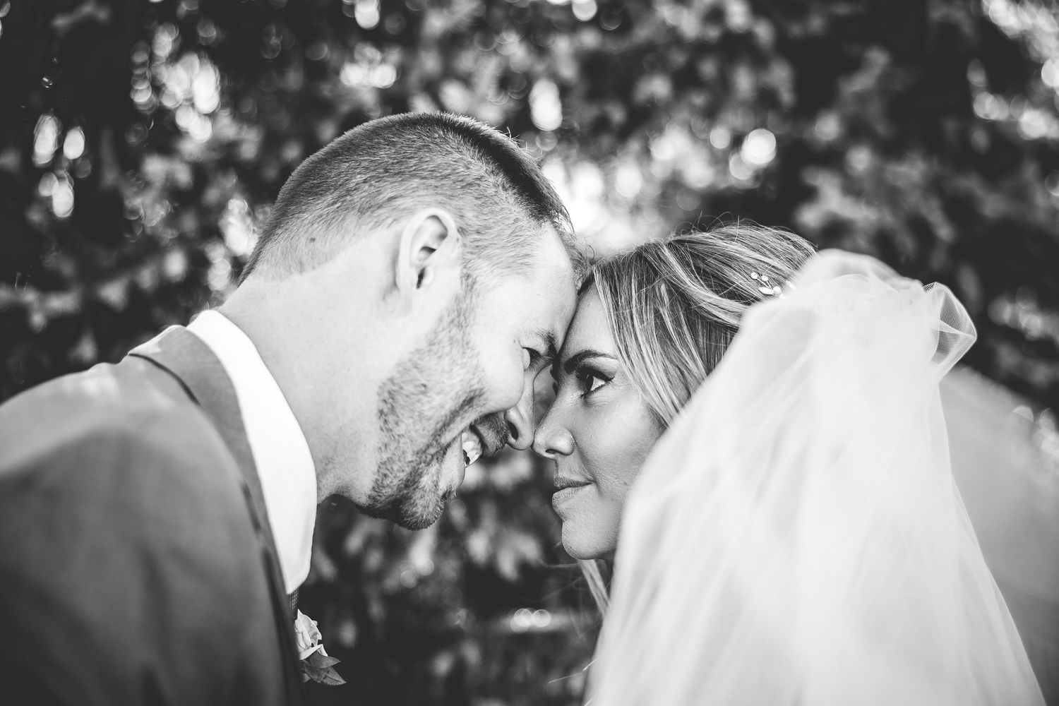 Intimate black and white portrait of newlyweds touching foreheads under bridal veil.