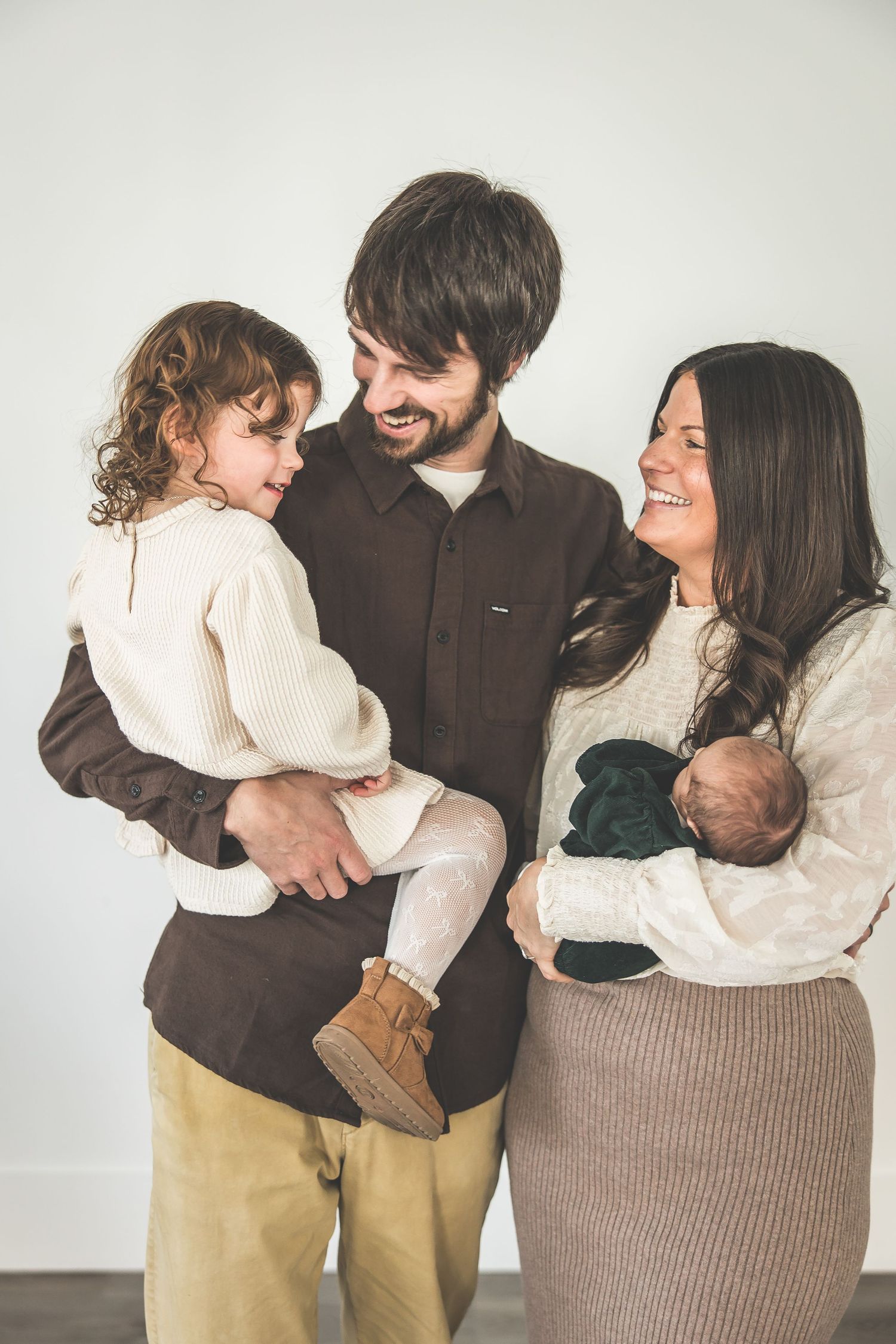 A family in casual clothing shares loving moments together against a white wall.