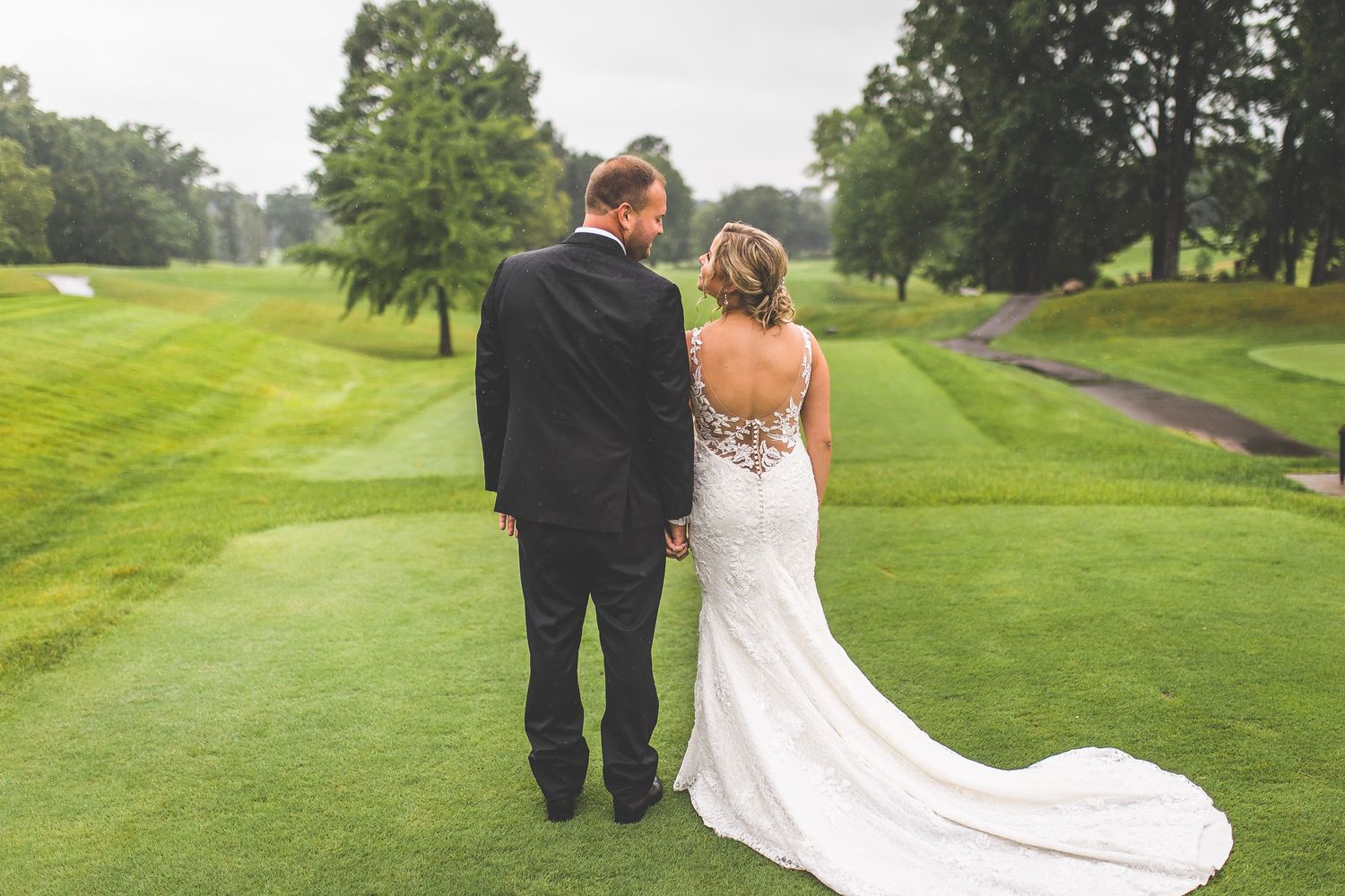 Newlyweds walk together on rolling green golf course.