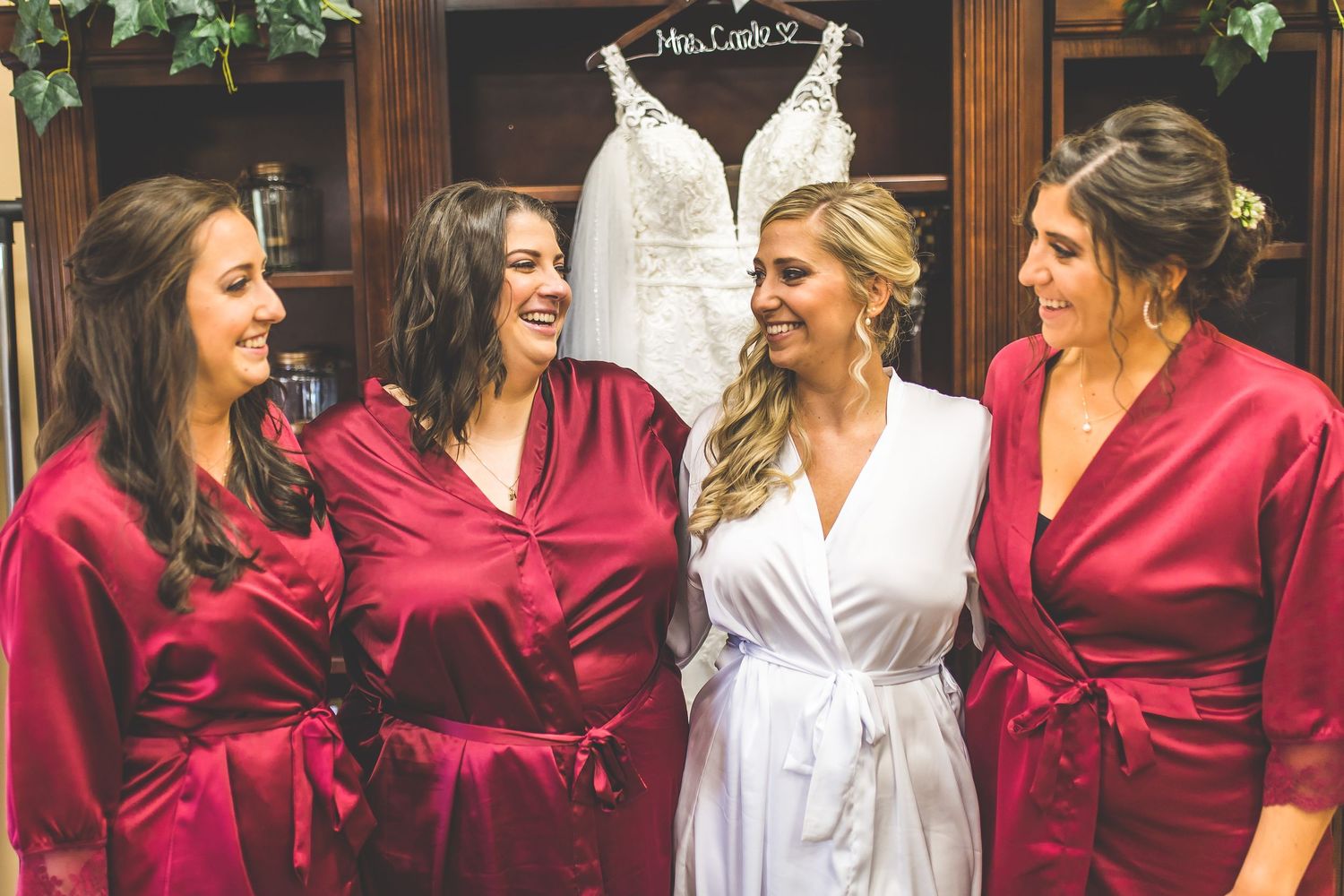 Bridal party in burgundy robes poses together during pre-wedding preparations.