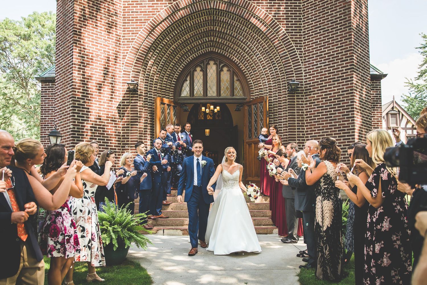 Wedding couple exits church through arched doorway as guests celebrate with confetti.