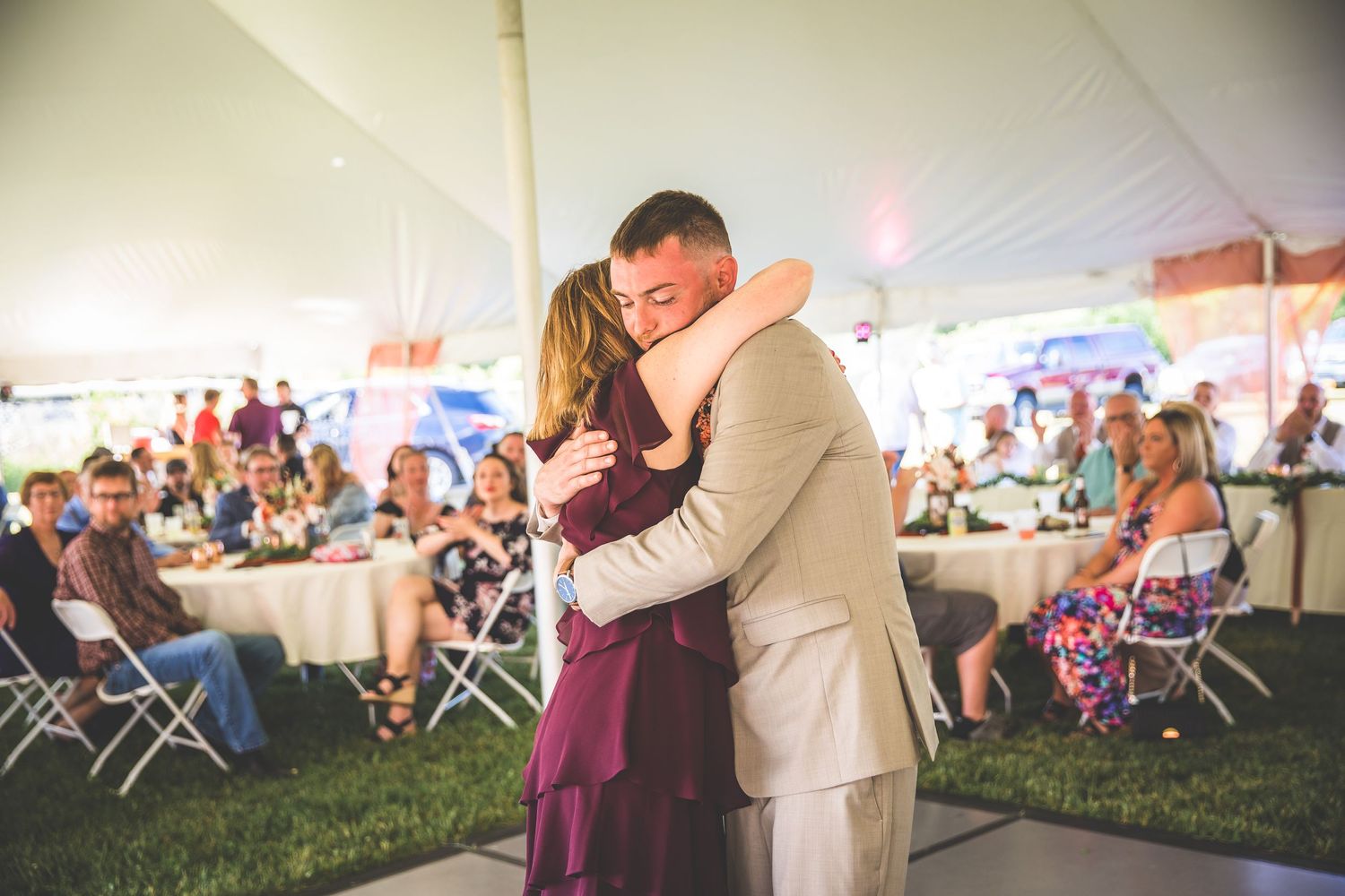 Couples dancing together at an outdoor wedding reception under a white tent.