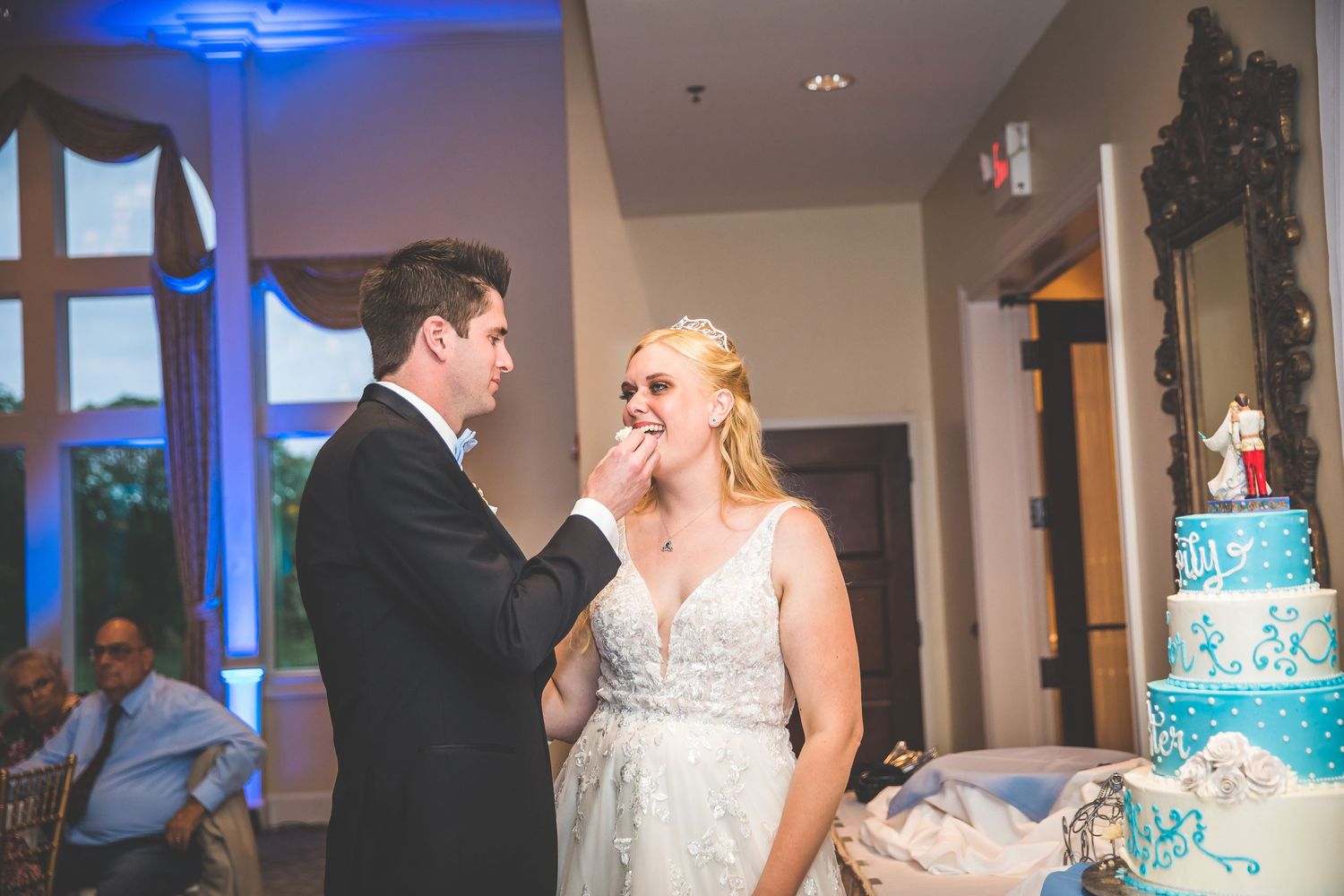Wedding couple embraces during their romantic first dance in a ballroom with blue accent lighting.