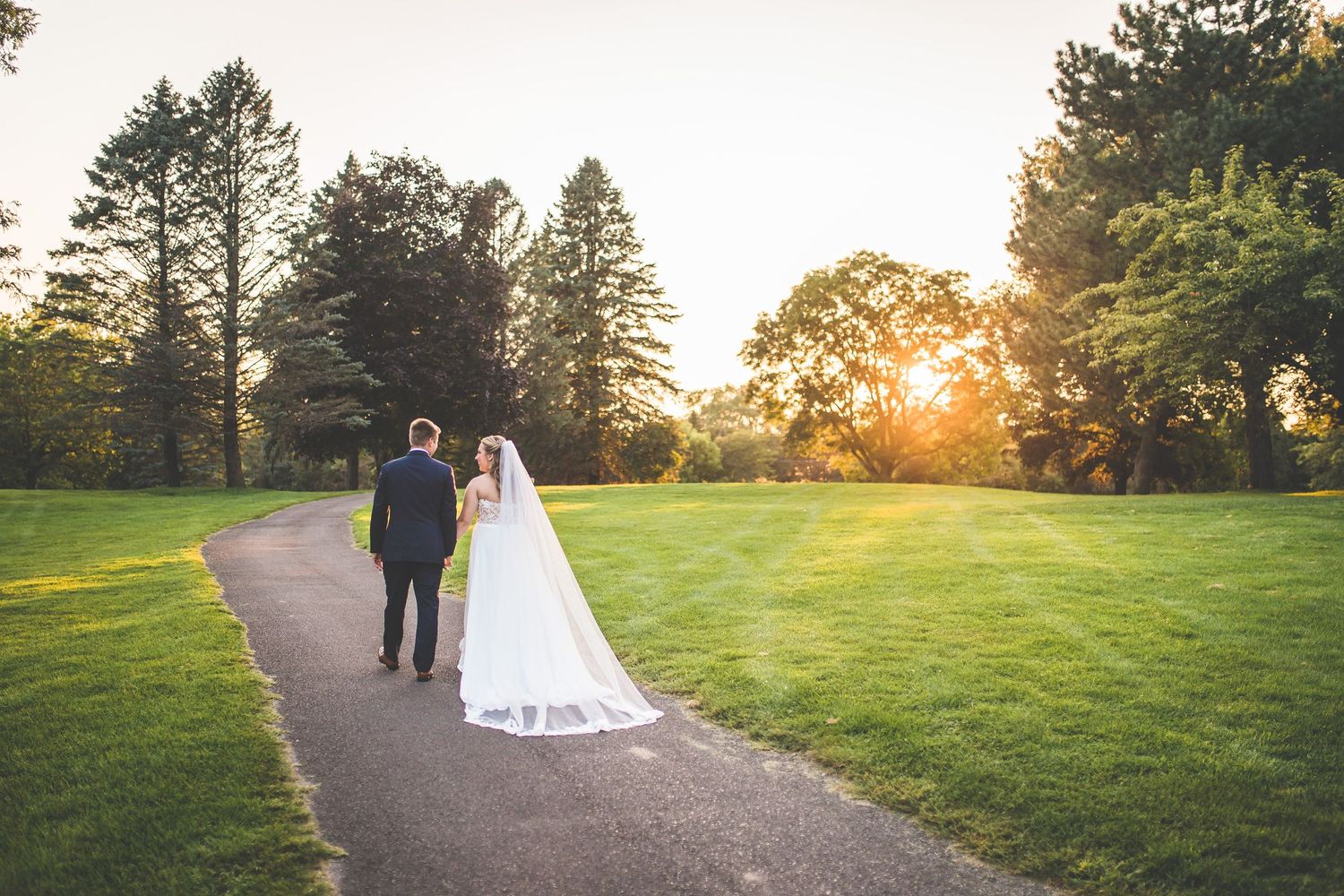 Romantic sunset wedding photos taken on a winding path through a grassy field.