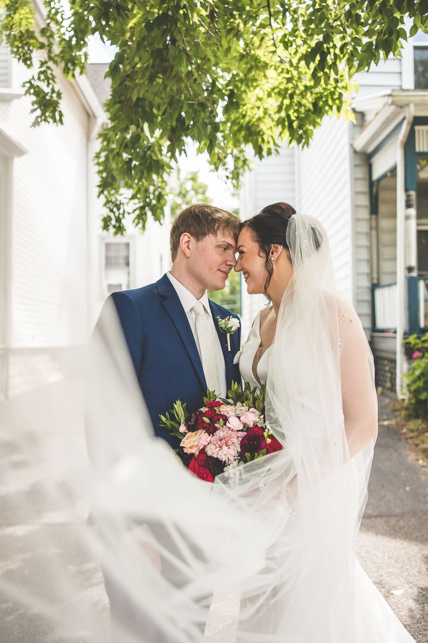 Romantic wedding moment captured under green leafy trees on sunny day.