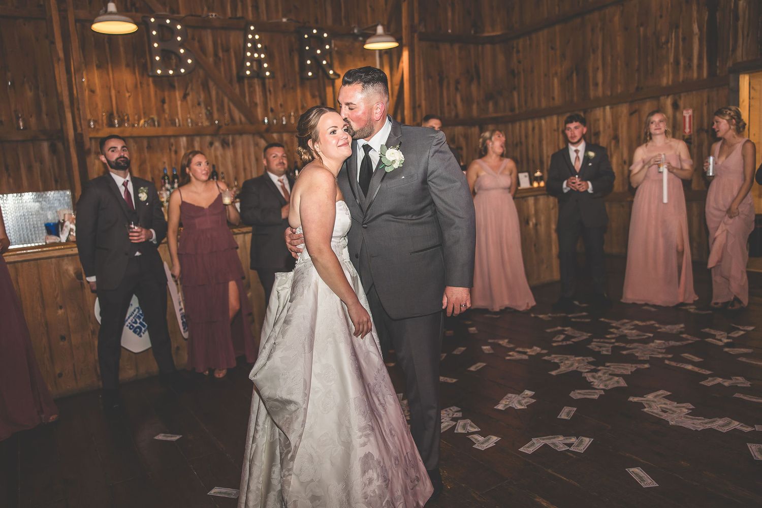 Wedding party and guests gathered in a beautifully decorated barn venue with string lights.