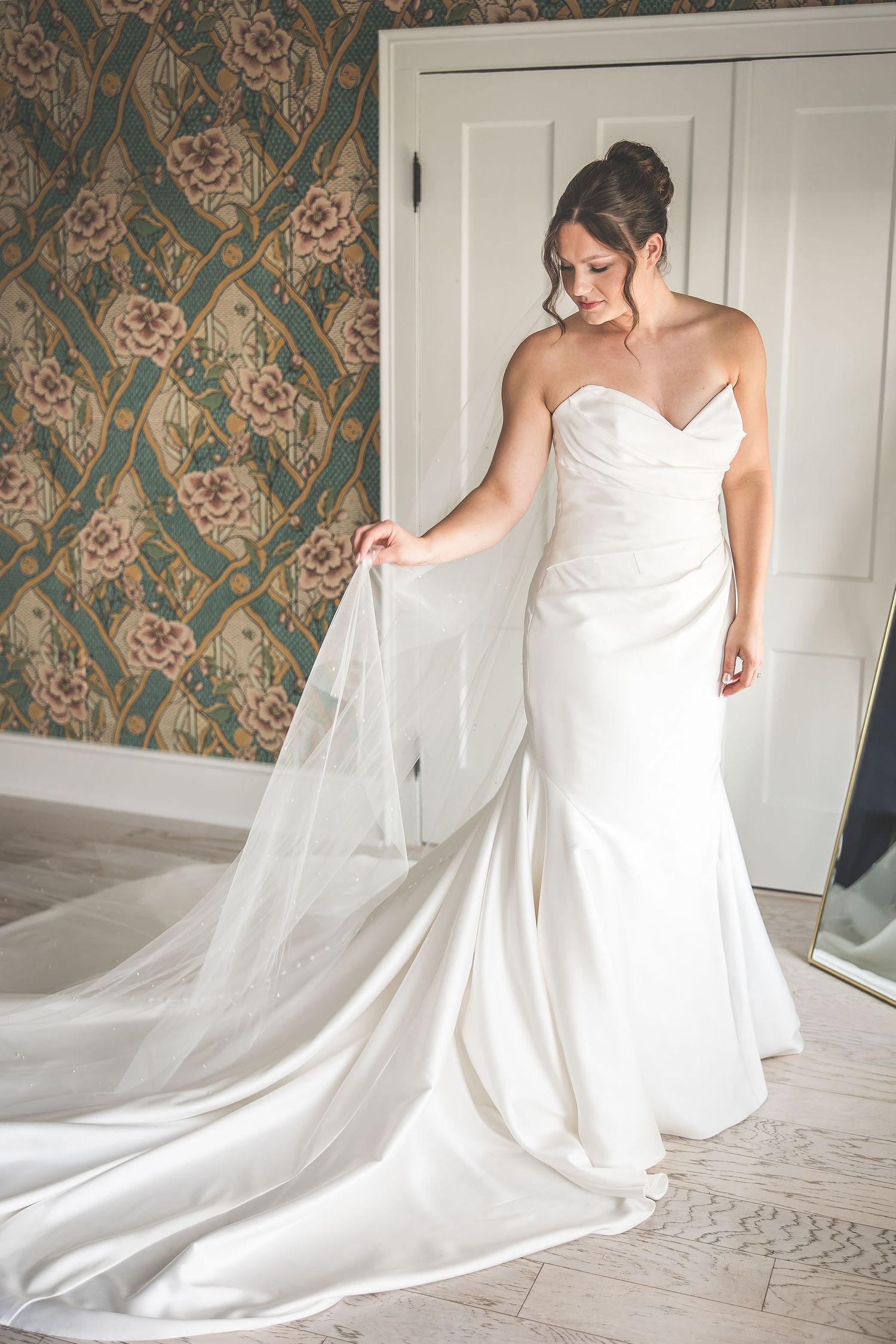 An elegant white wedding gown with a flowing train against patterned wallpaper.