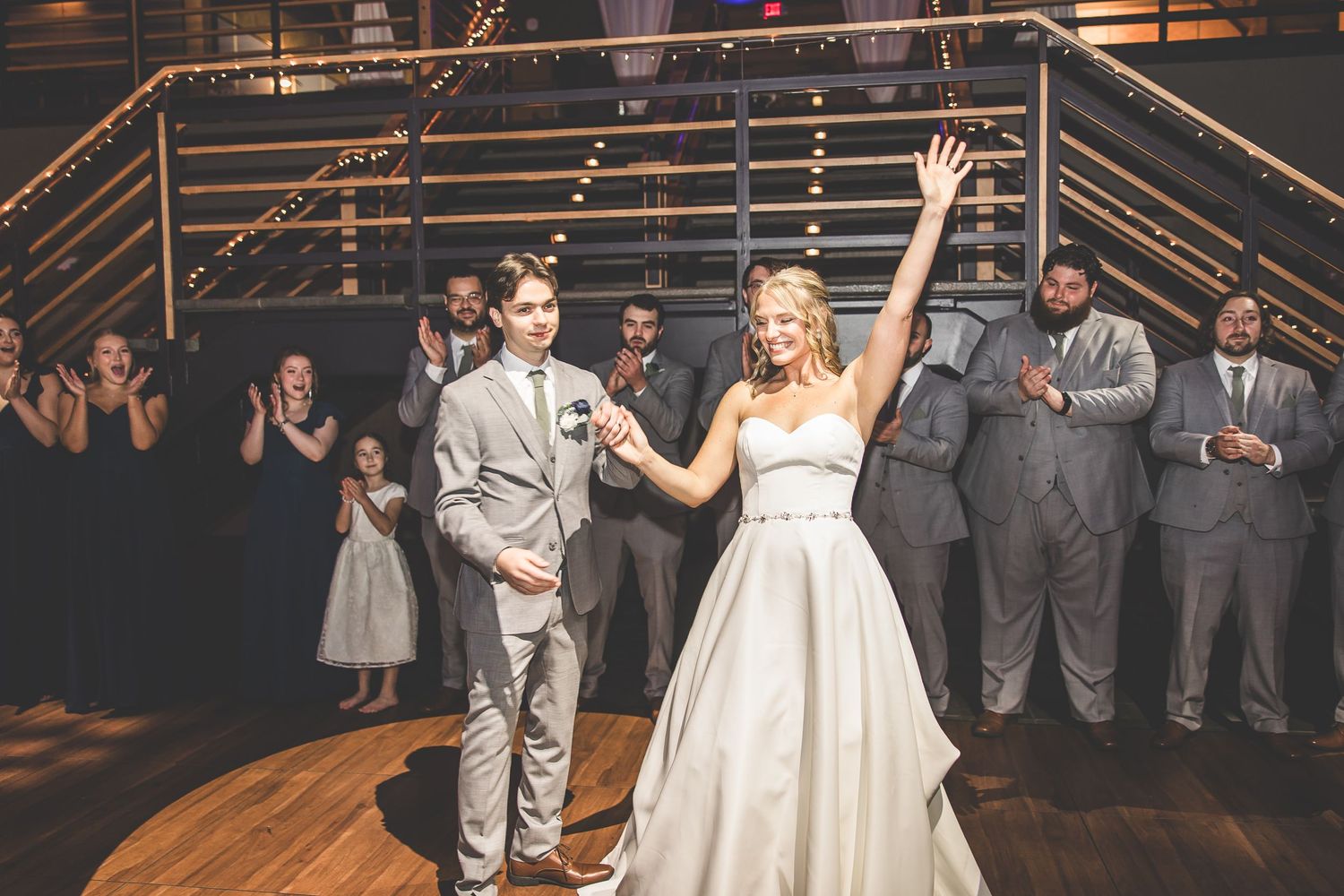 A joyful celebration moment during a wedding reception on a wooden dance floor with the wedding party watching.