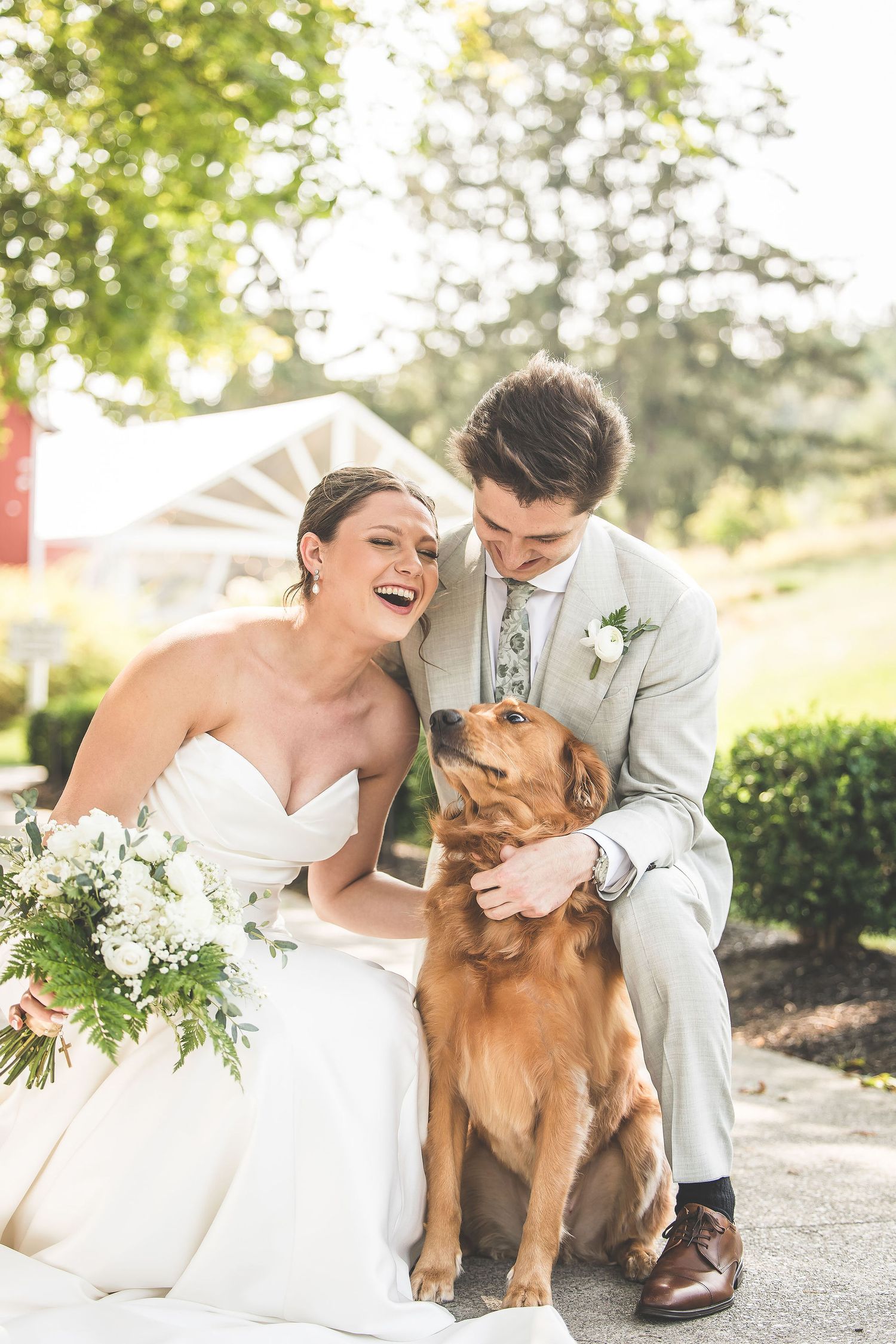 A couple shares a joyful moment with their golden retriever during wedding photos.
