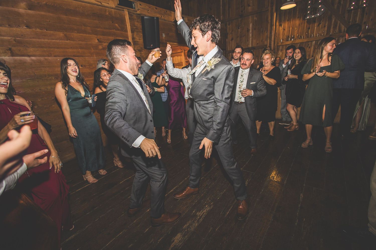 Party crowd dancing and celebrating in a rustic barn reception venue with wooden walls.
