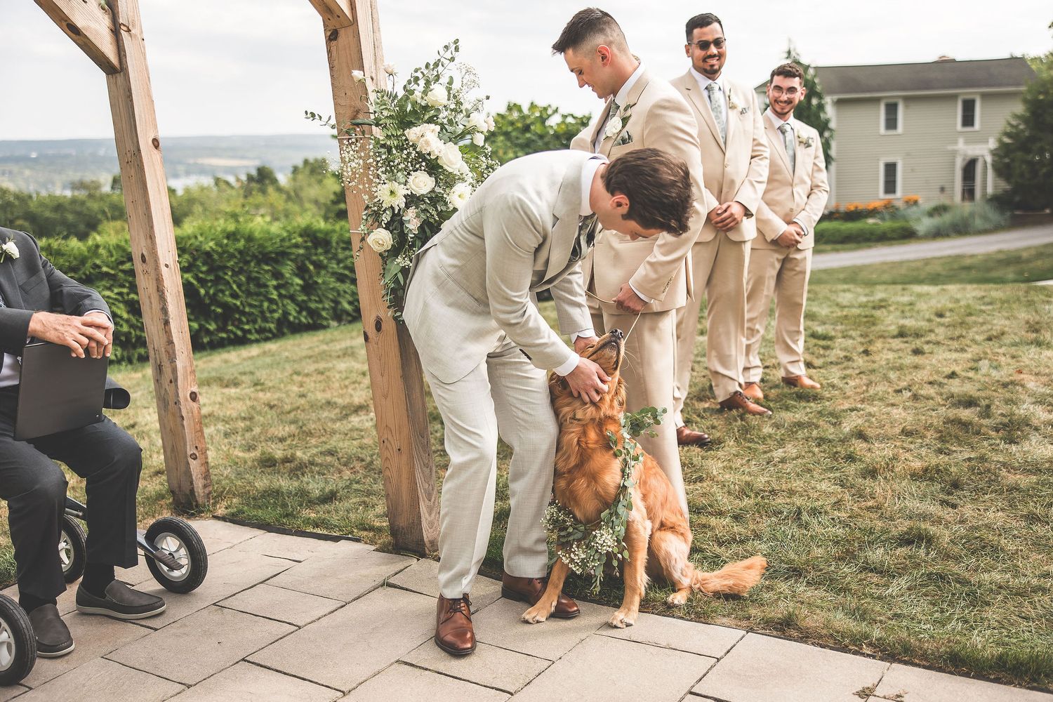 Dog participates in outdoor wedding ceremony on stone pathway under wooden arch.