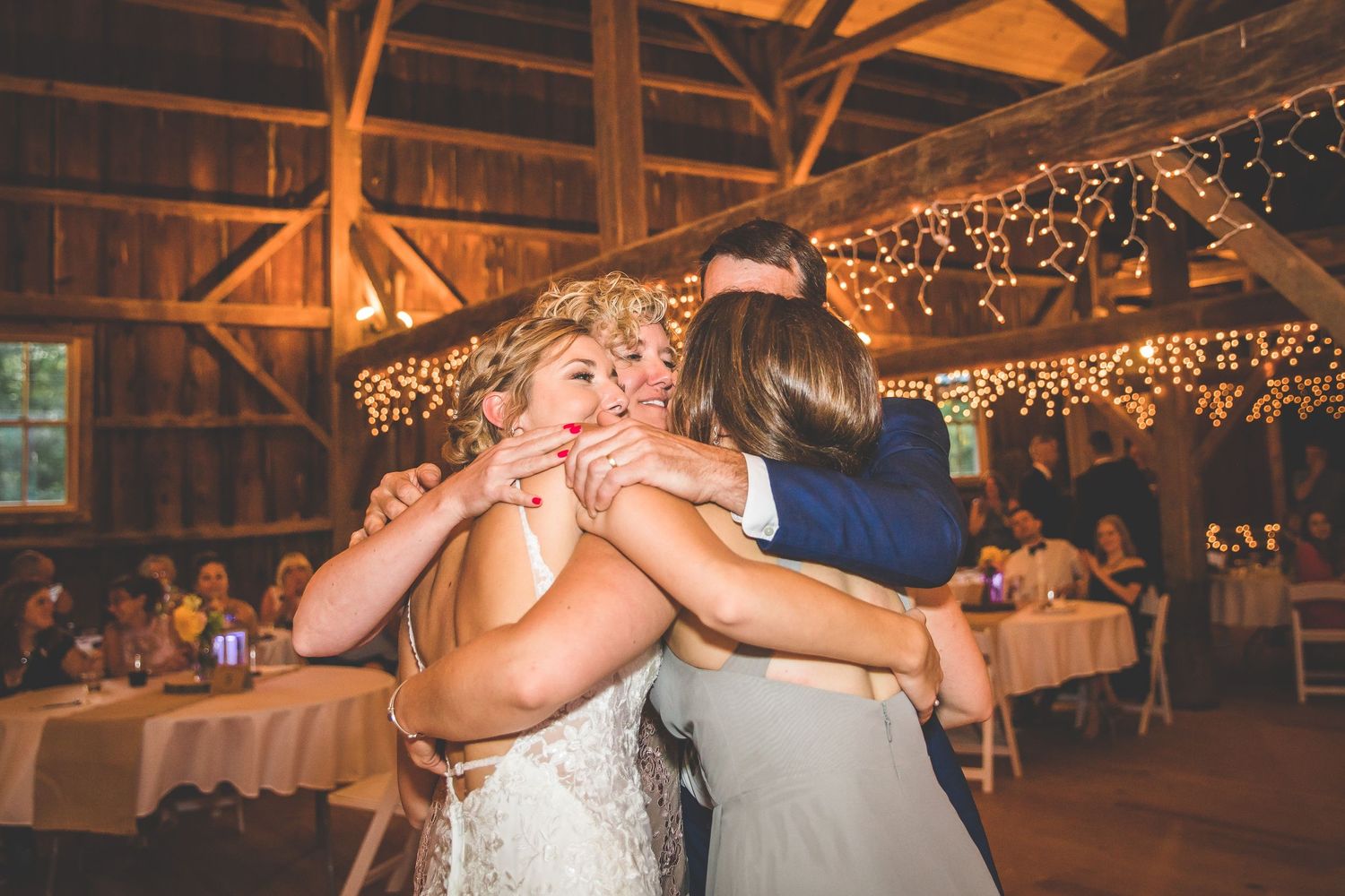 Rustic barn wedding reception with string lights illuminating wooden beams and dance floor.