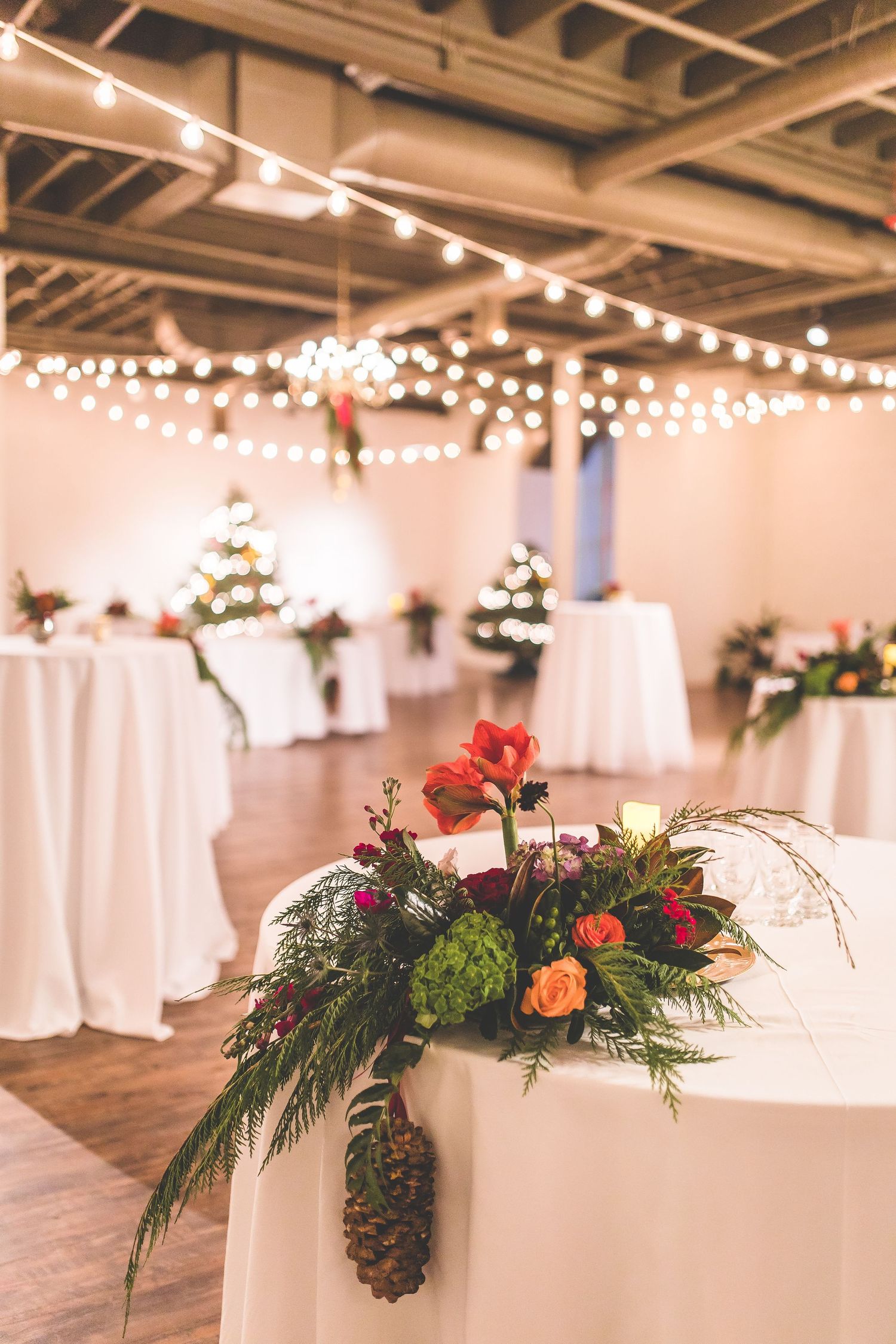 White wedding reception tables decorated with evergreen and floral centerpieces under string lights.