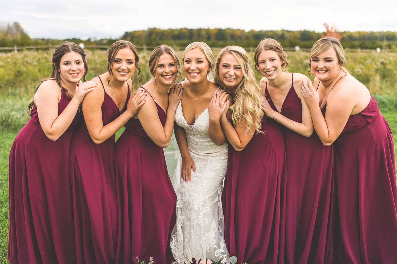 Wedding party poses in burgundy and navy attire on a grassy field.