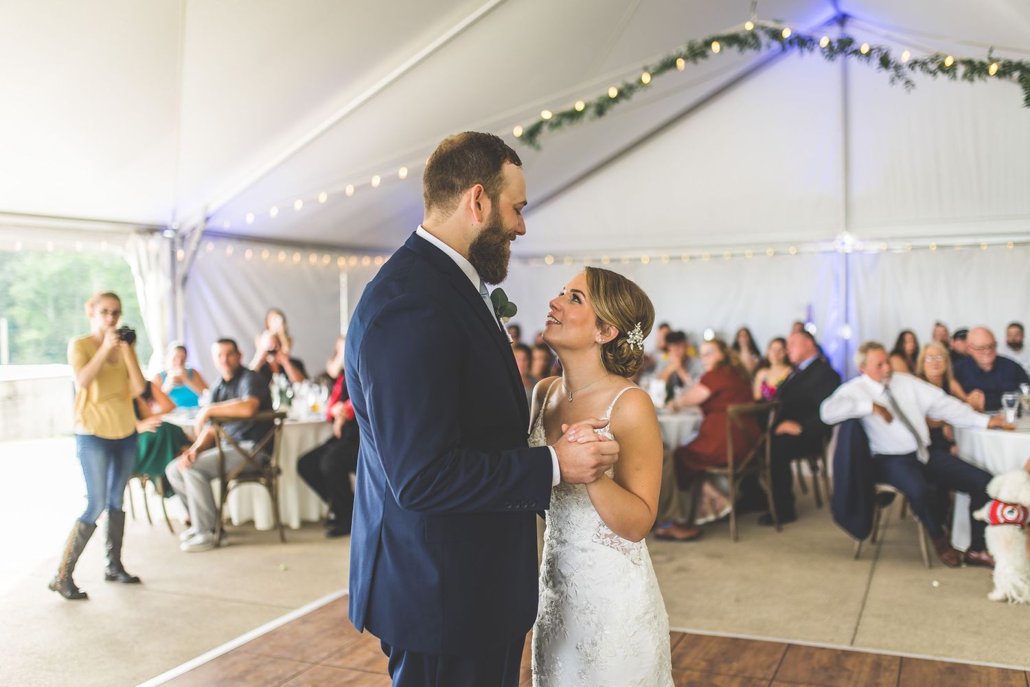 Wedding couple dances together under string lights in an outdoor tent reception.
