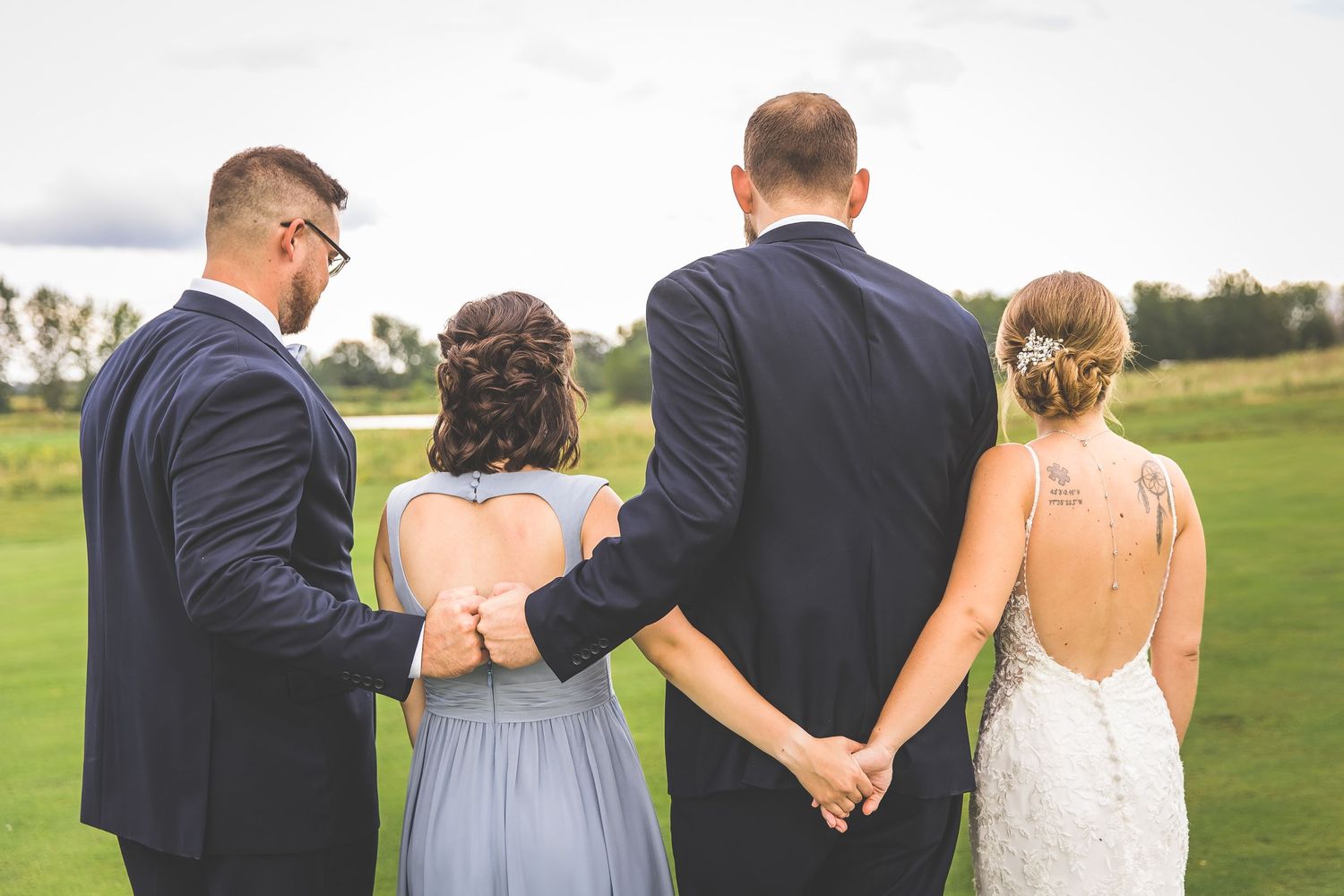 Wedding party members stand arm in arm on a scenic golf course overlooking the landscape.