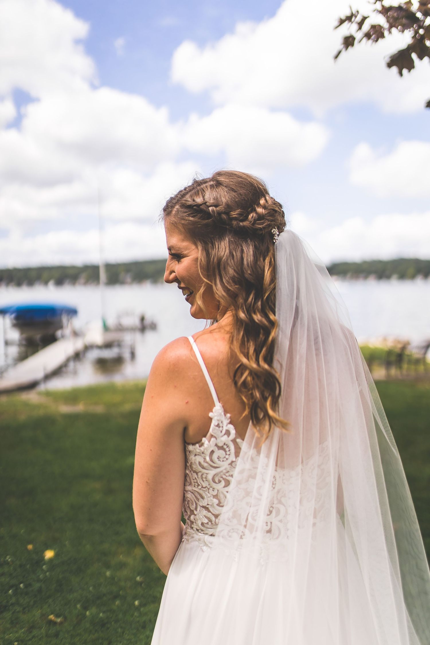 Detailed lace back of white wedding dress with flowing veil against blue sky background.