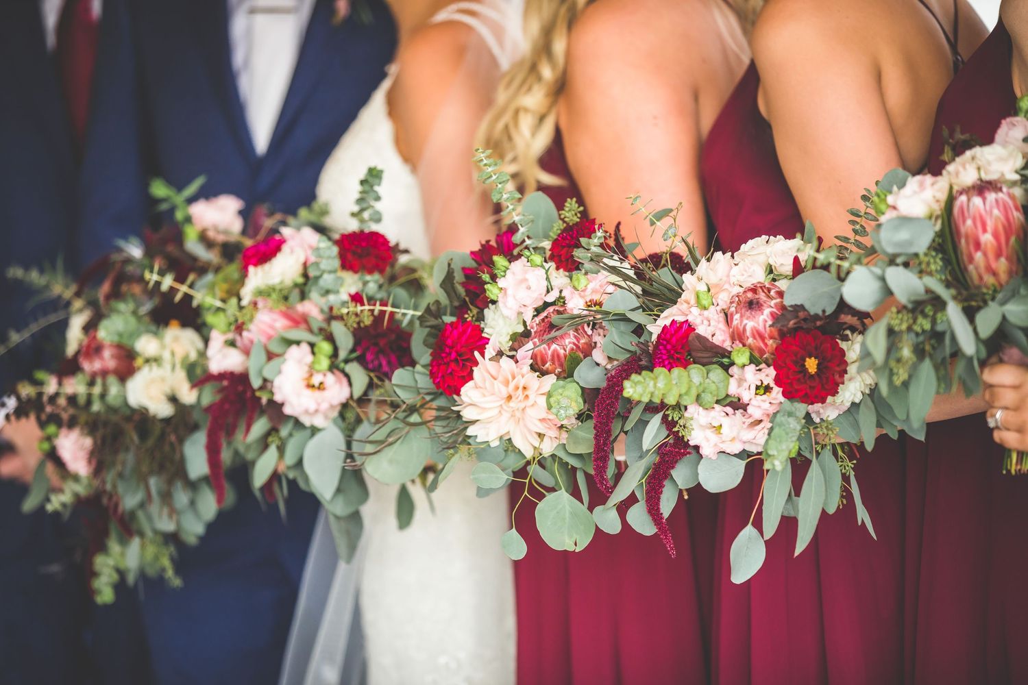 Close-up of wedding bouquets featuring pink roses, burgundy flowers, and eucalyptus greenery.