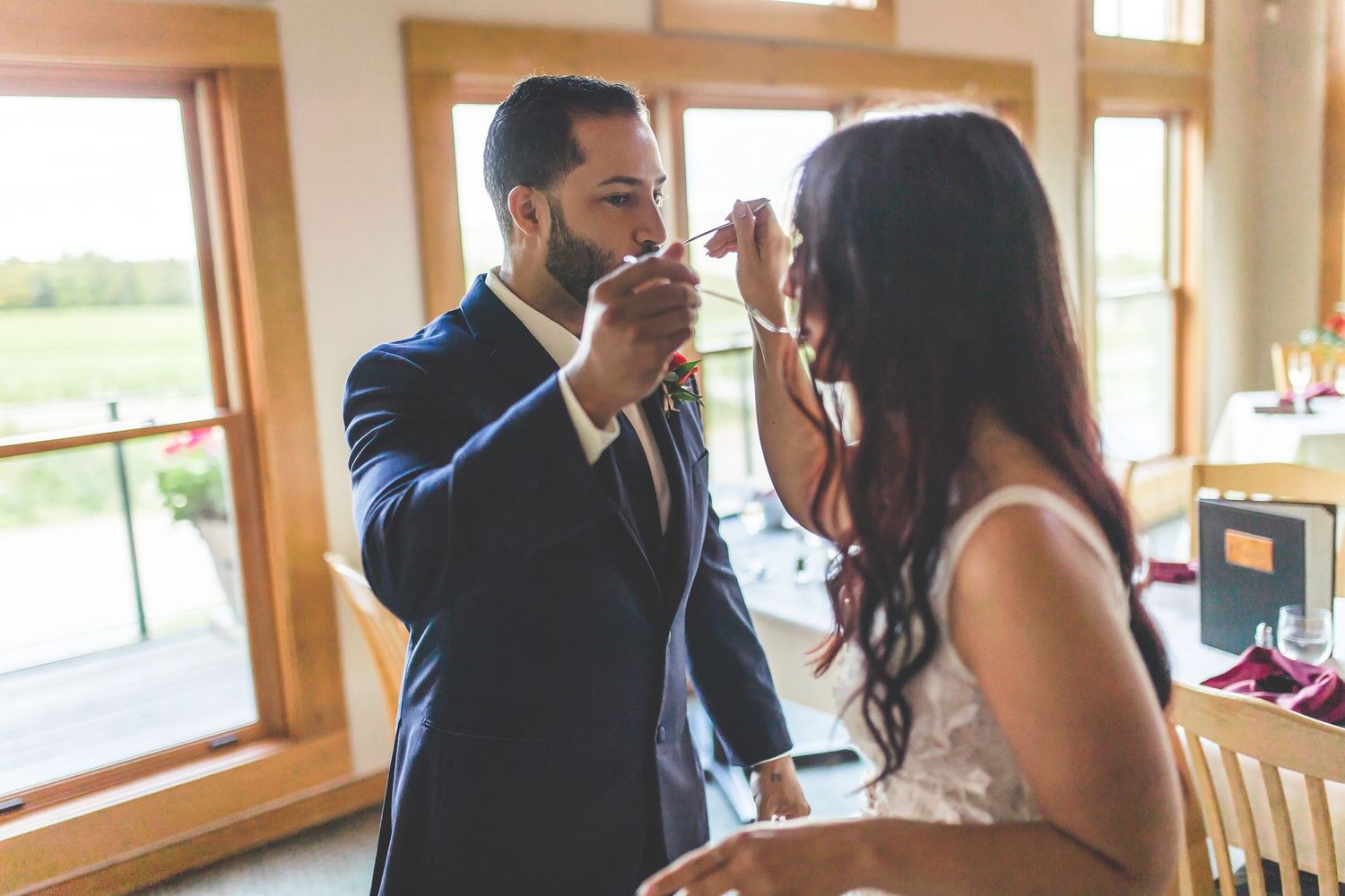 Couple in formal attire sharing a romantic moment by sunlit windows.