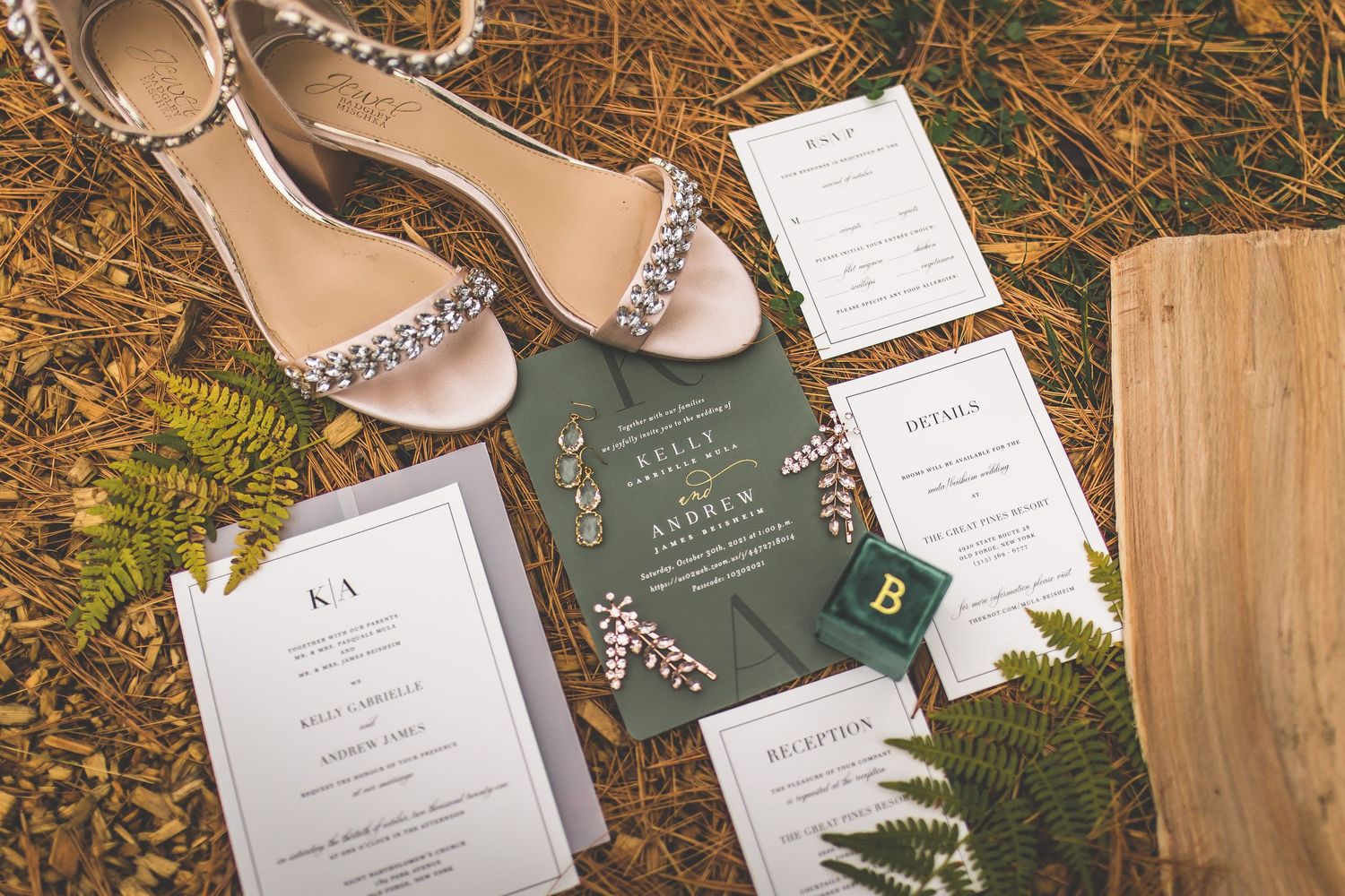 Wedding details including sparkly sandals, invitation suite, and greenery arranged on natural ground.
