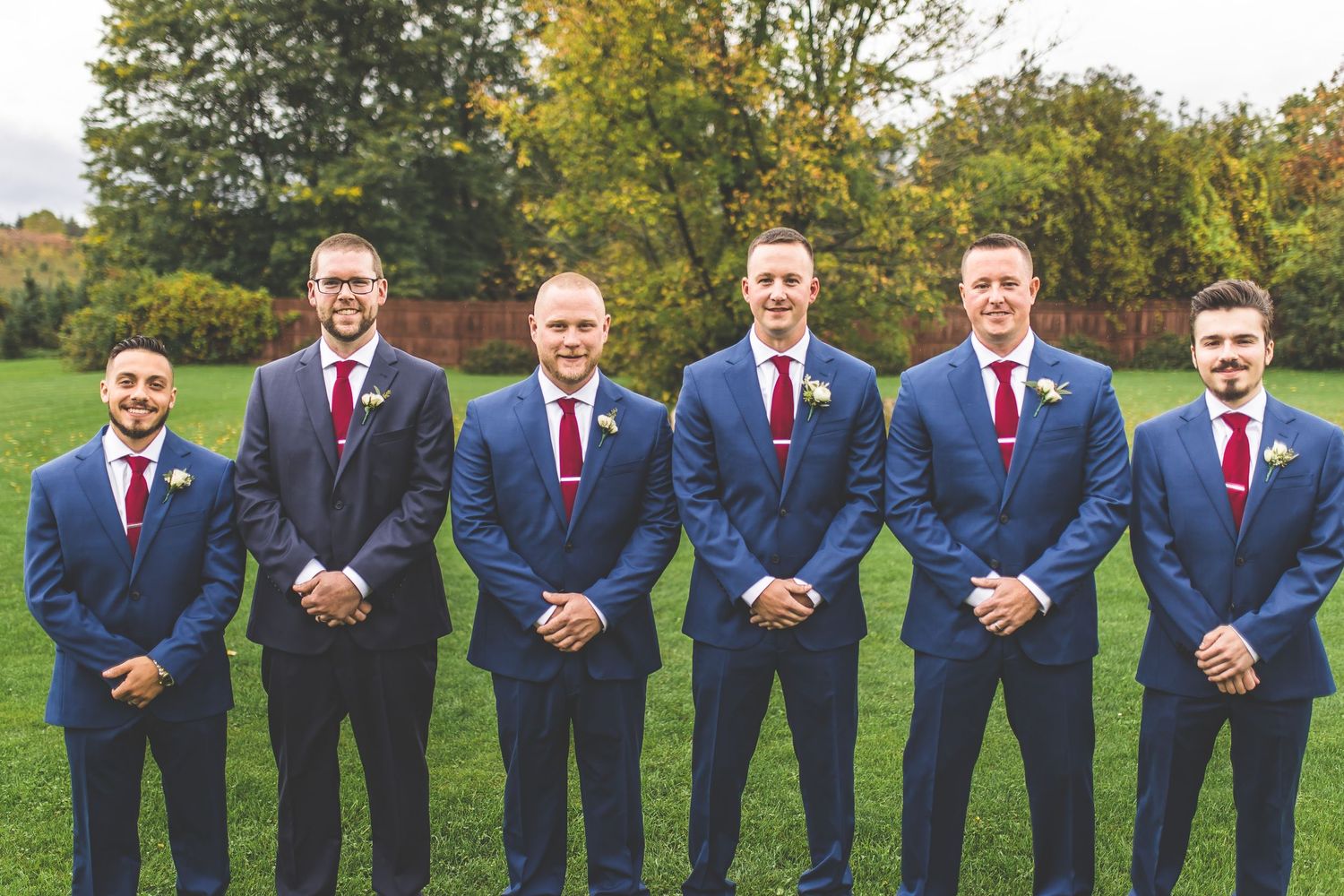 Groomsmen in navy suits and burgundy ties lined up outdoors for formal wedding photo.