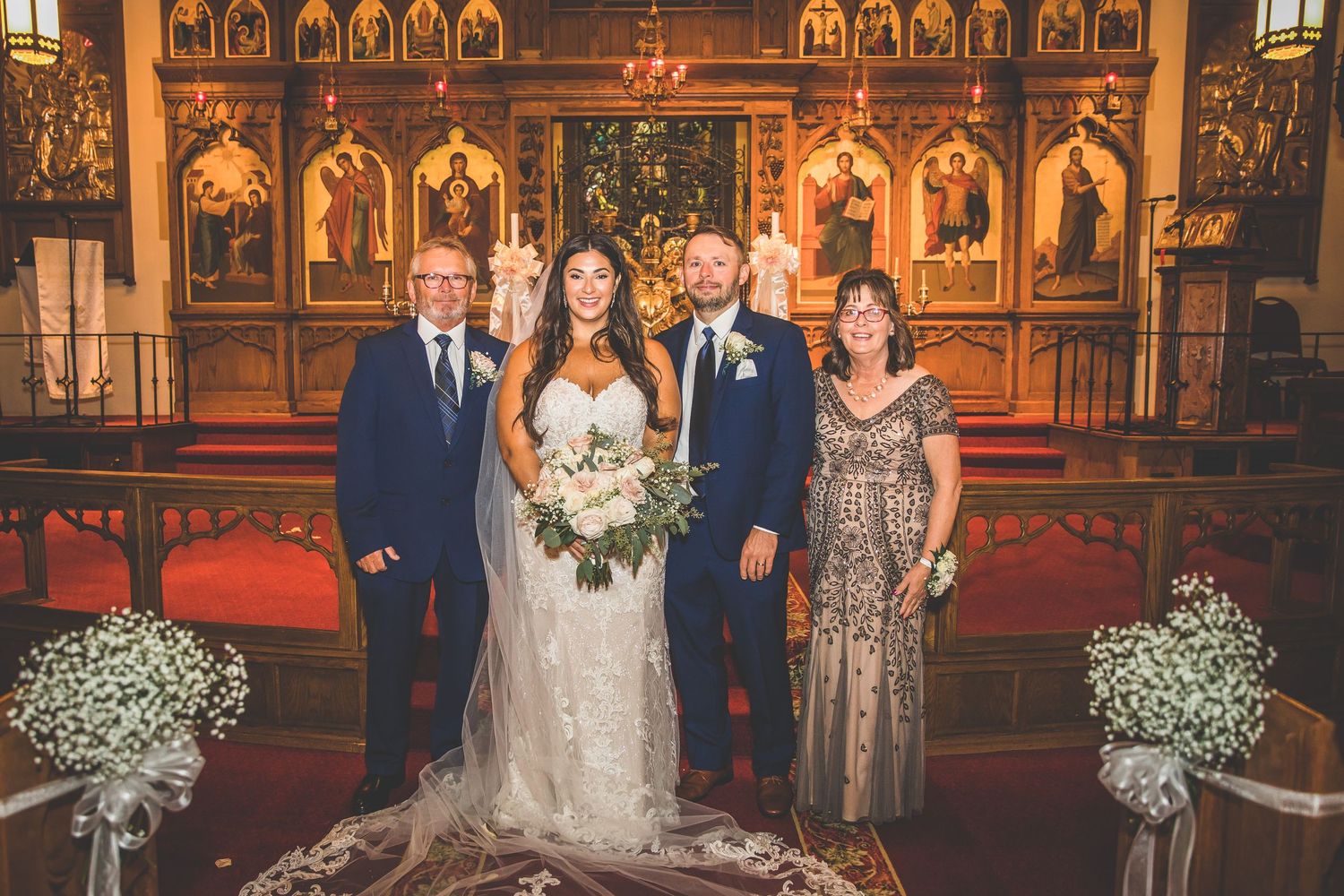 Wedding party and family members gather for formal photos in front of decorated church altar.