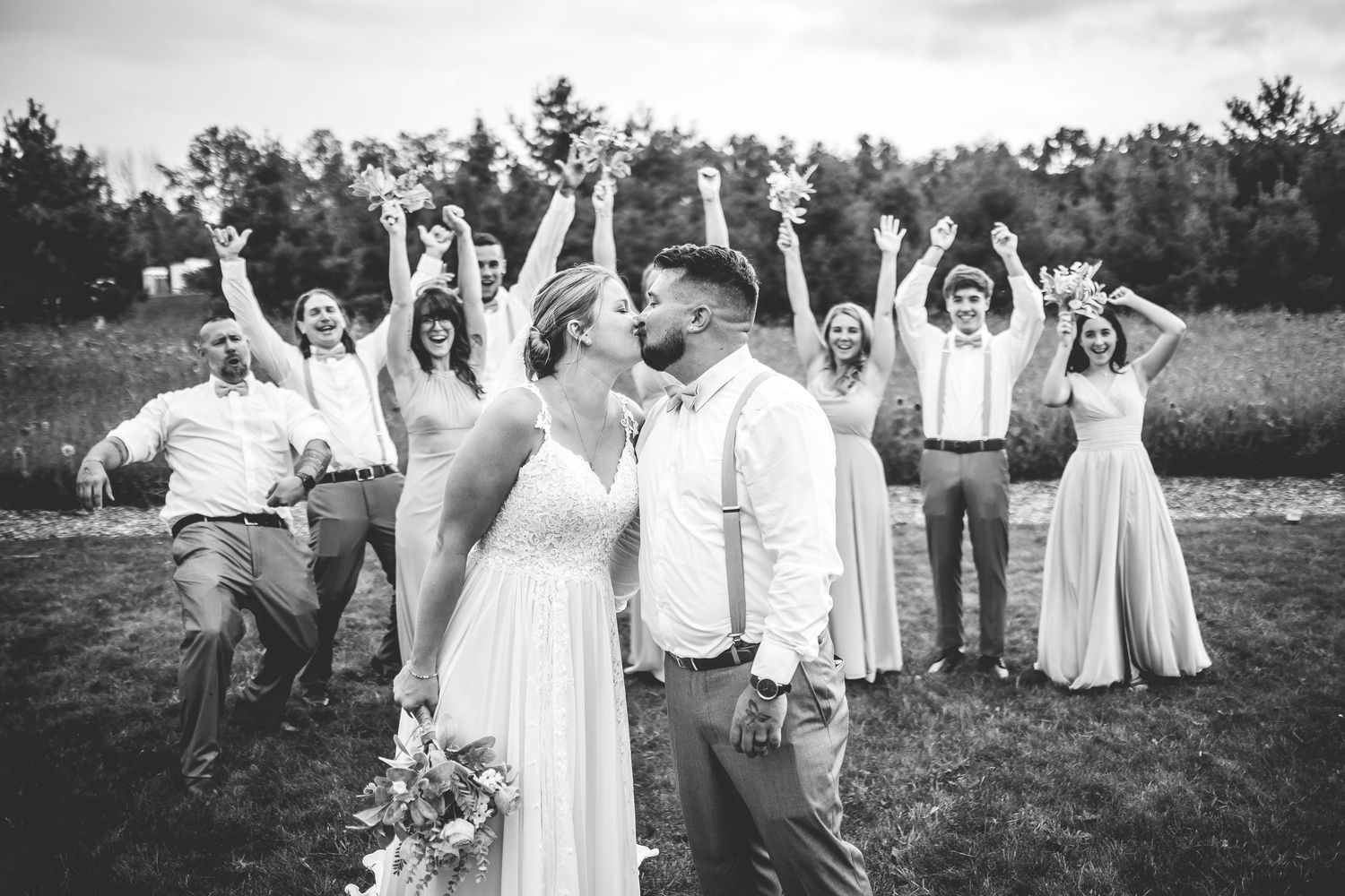 Black and white photo of wedding party members with arms raised in celebration outdoors.