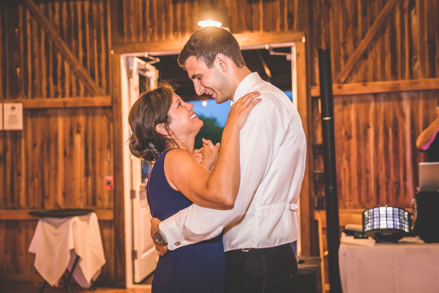 Wedding guests dancing and celebrating in a rustic wooden barn with ambient lighting.