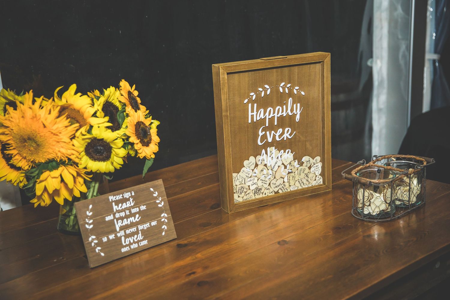 Wedding decor featuring wooden signs and sunflowers on a dark wooden table.