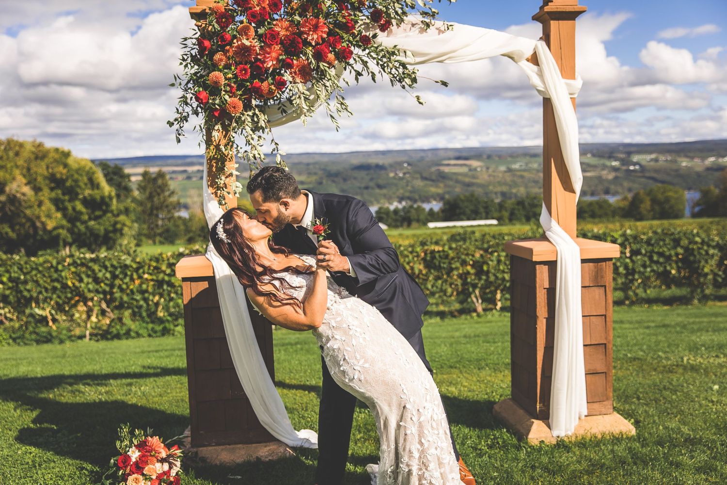 Scenic vineyard wedding ceremony with decorated wooden arch and white draping.