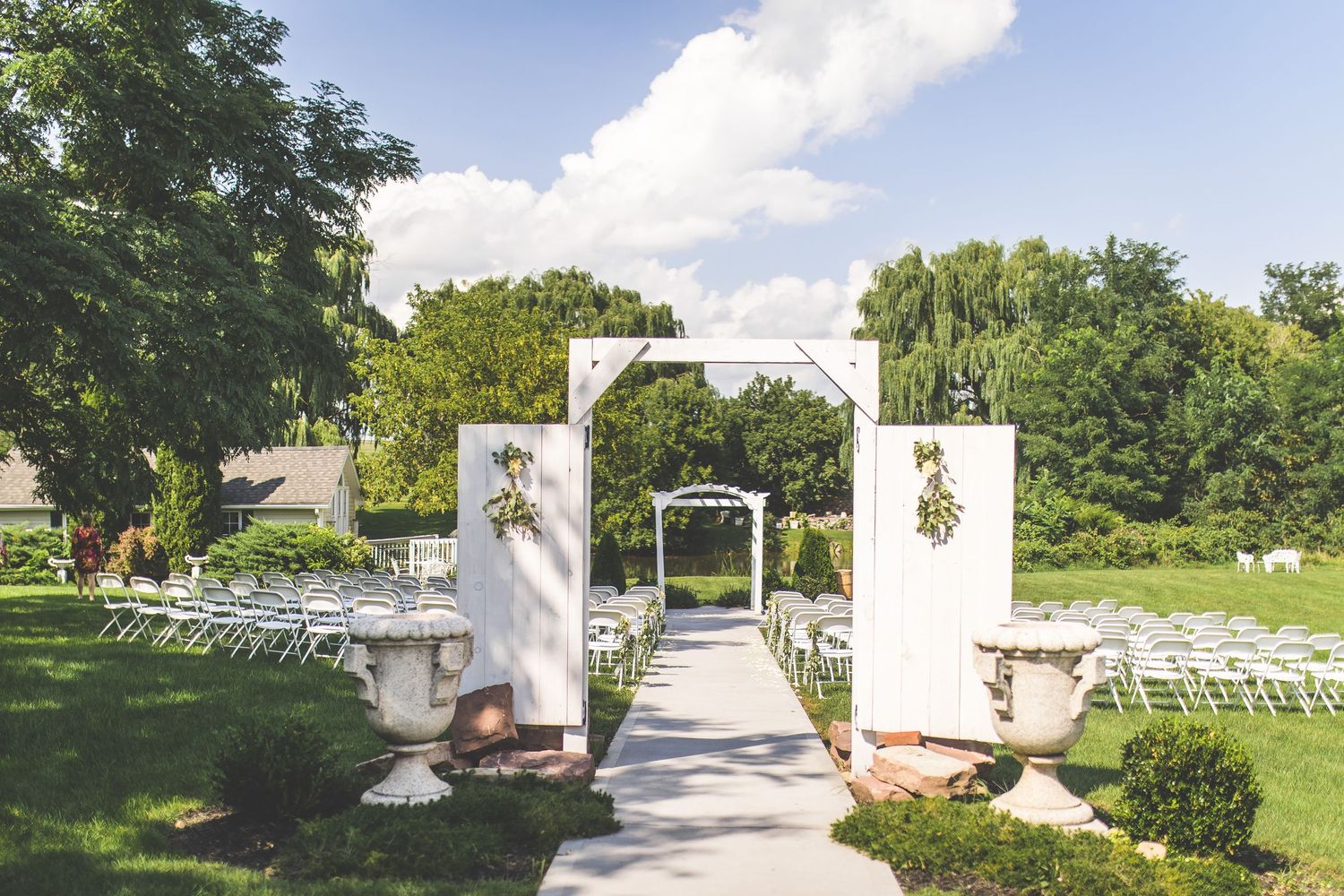 Outdoor wedding ceremony setup with white chairs and floral arch against blue sky.