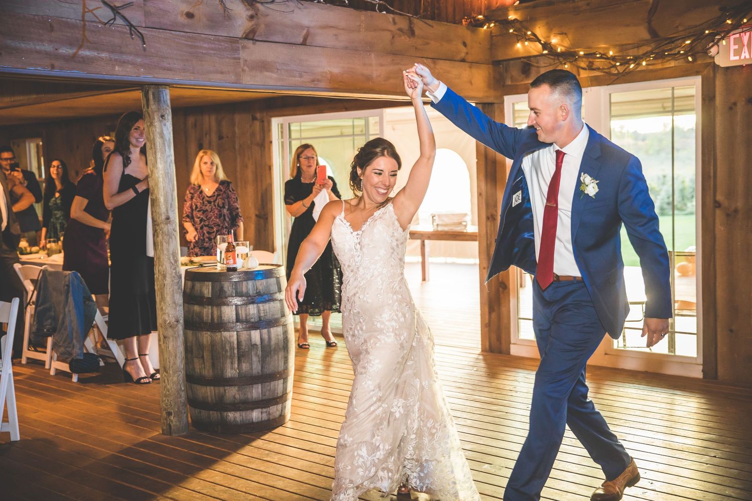 Wedding party dances and celebrates in a warmly lit rustic barn setting.