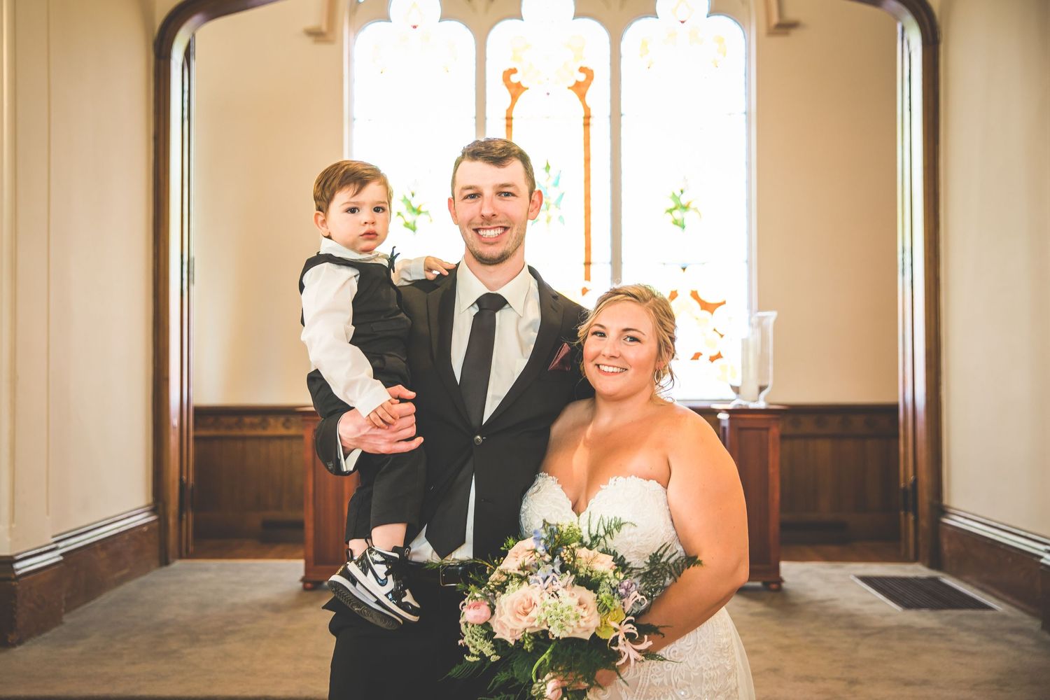 Wedding portrait in front of stained glass windows inside a traditional church.