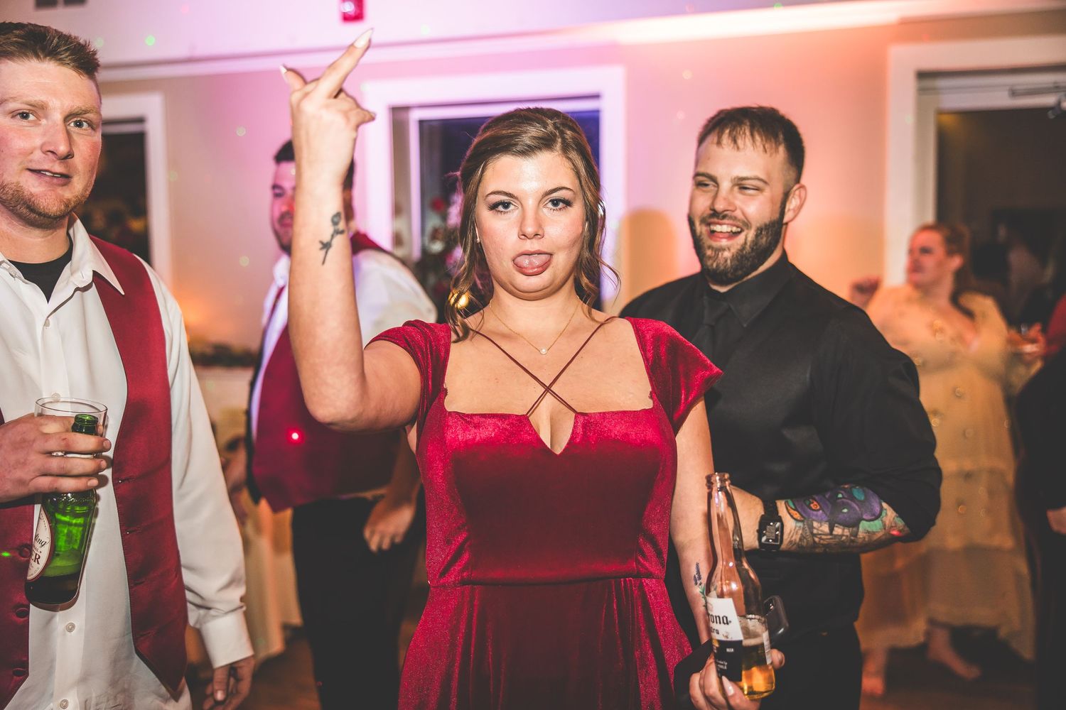Wedding guests enjoying themselves on a dance floor with pink ambient lighting.