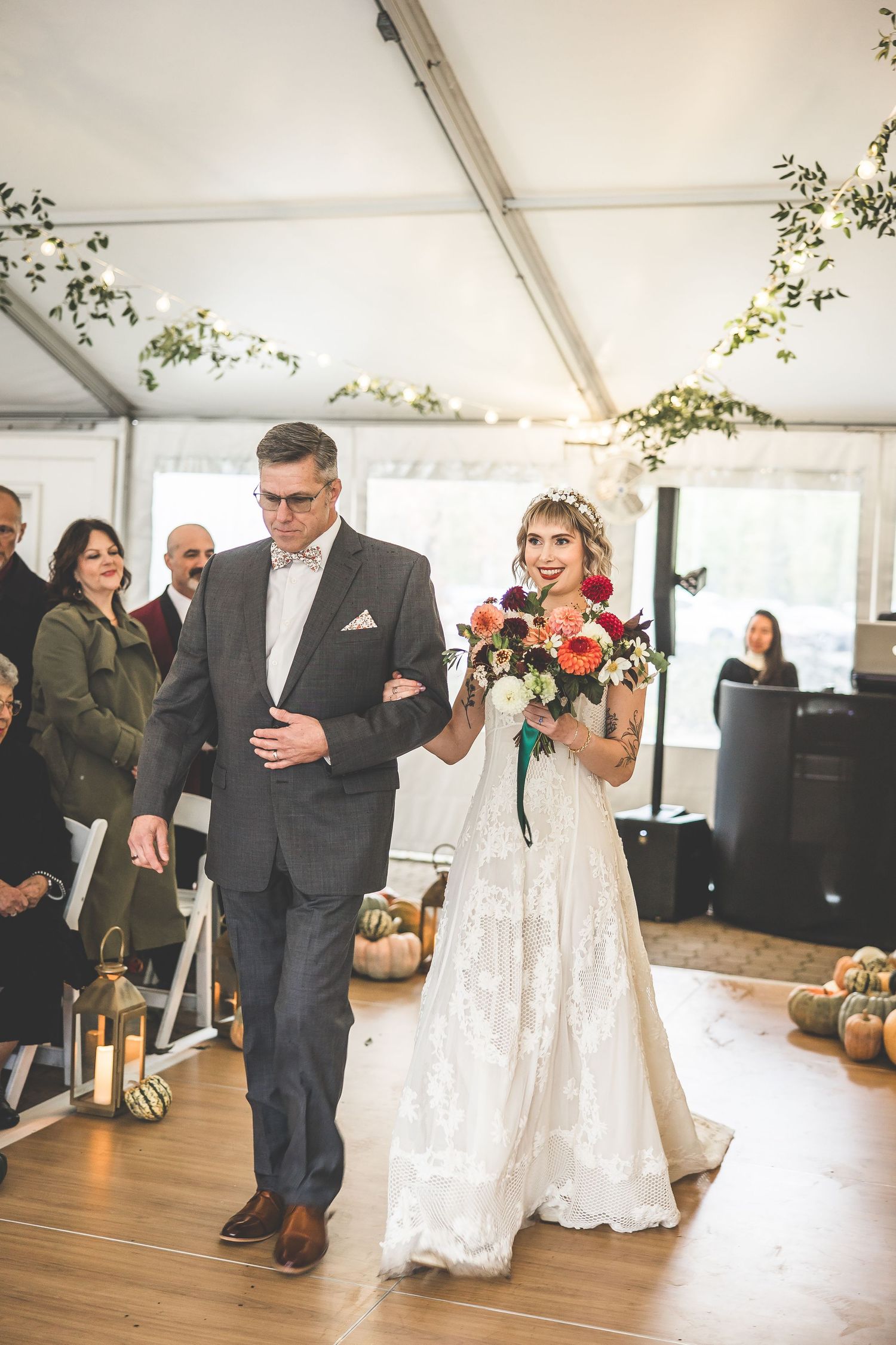 A wedding ceremony in a white tent venue with string lights and floral decorations.
