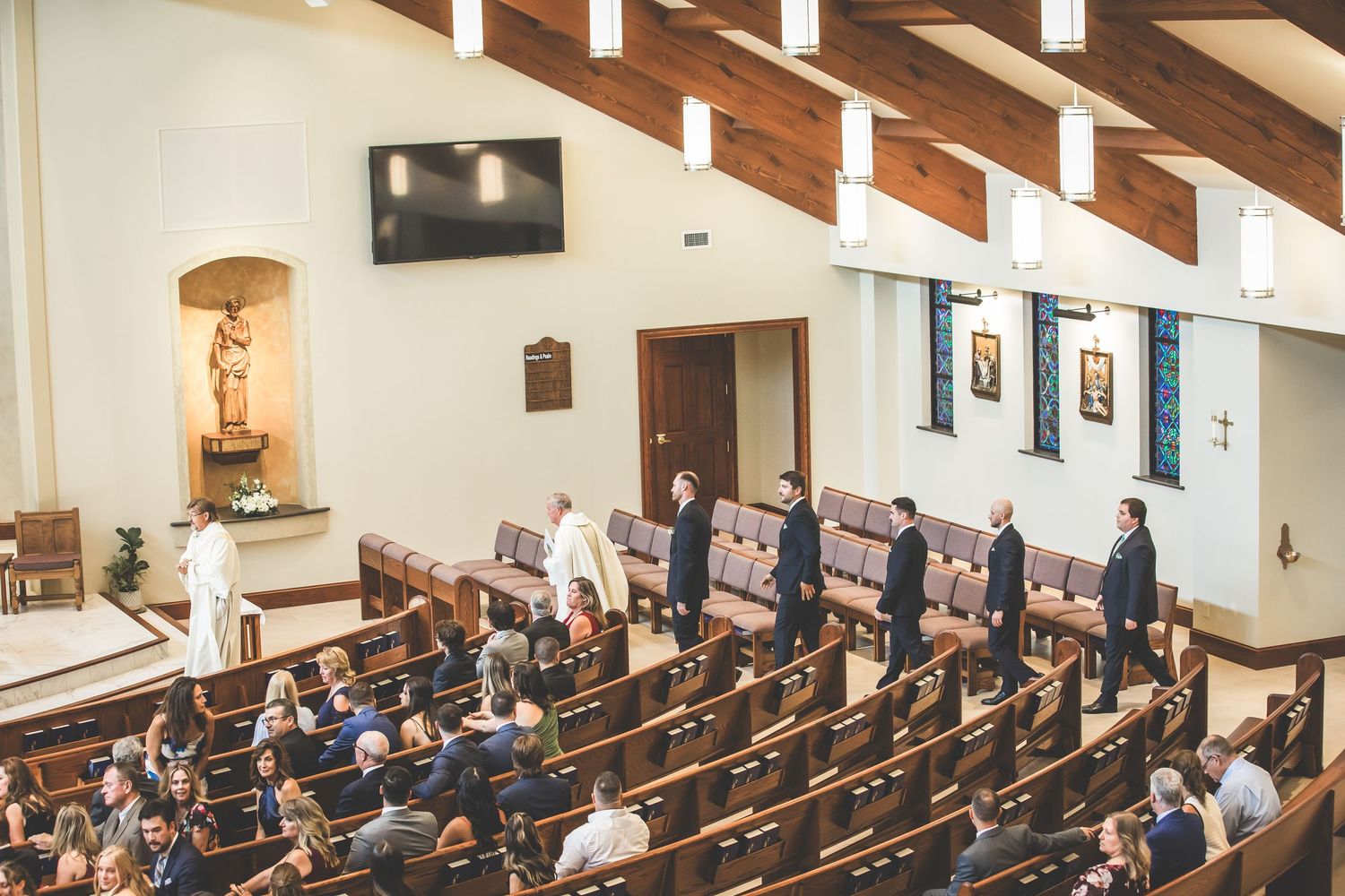 Wedding ceremony in progress showing guests seated in wooden pews under exposed beam ceiling.