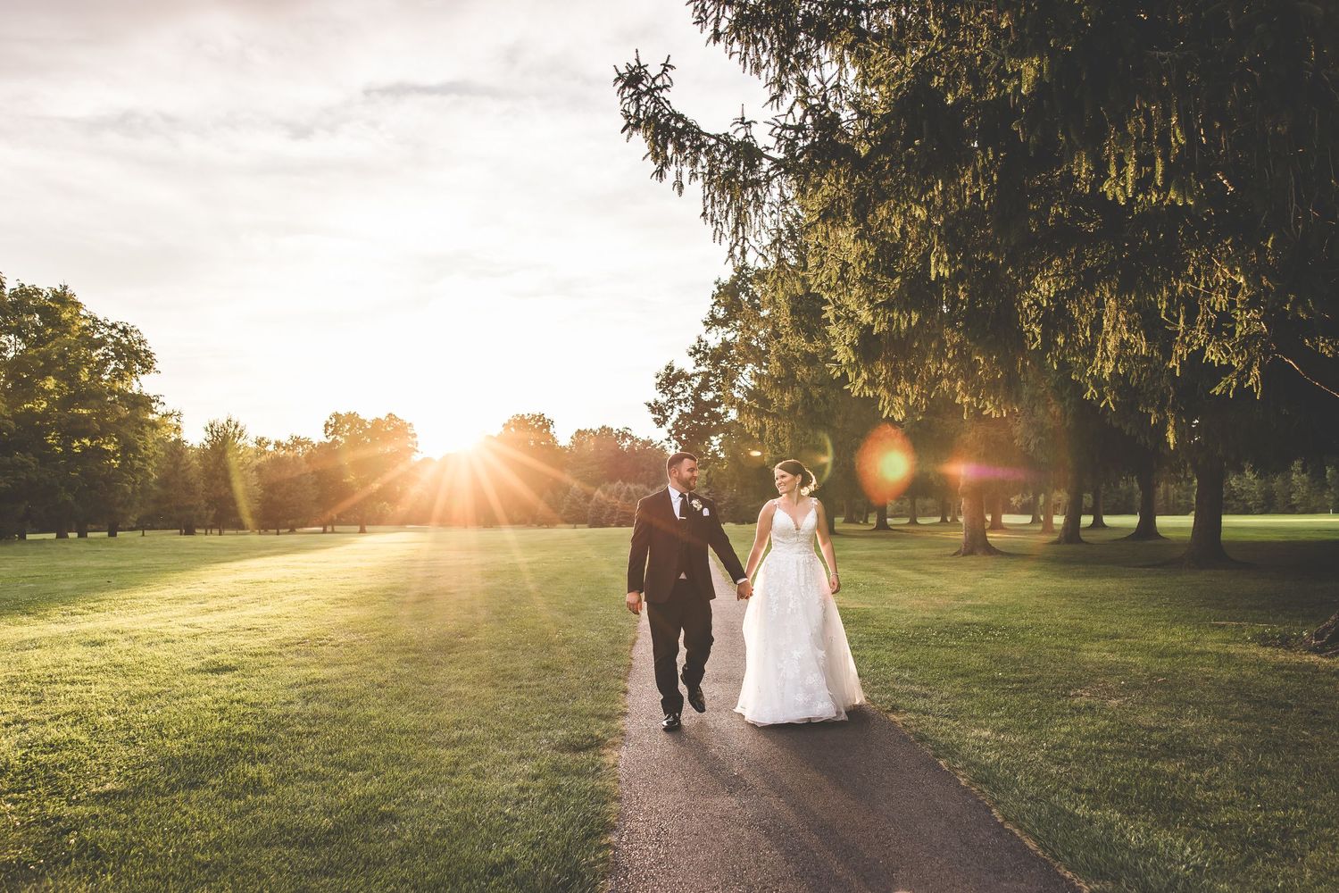 Wedding couple walks hand in hand across a scenic golf course at dusk.