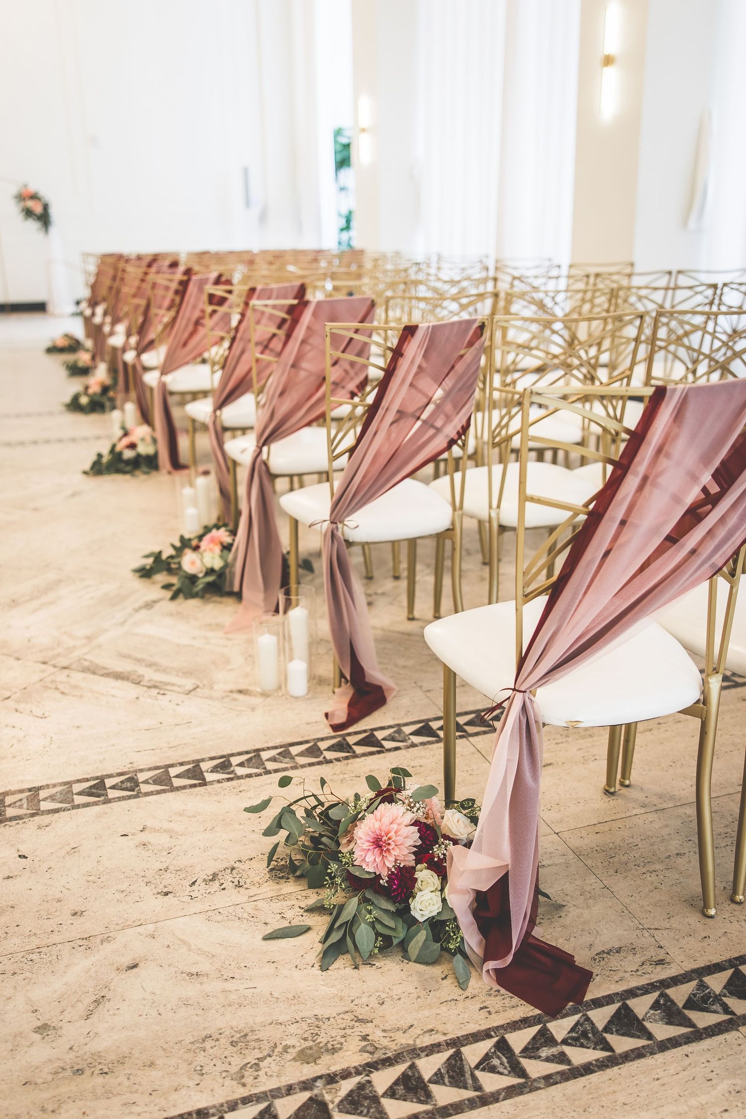 Wedding ceremony chairs decorated with dusty rose fabric and floral arrangements.