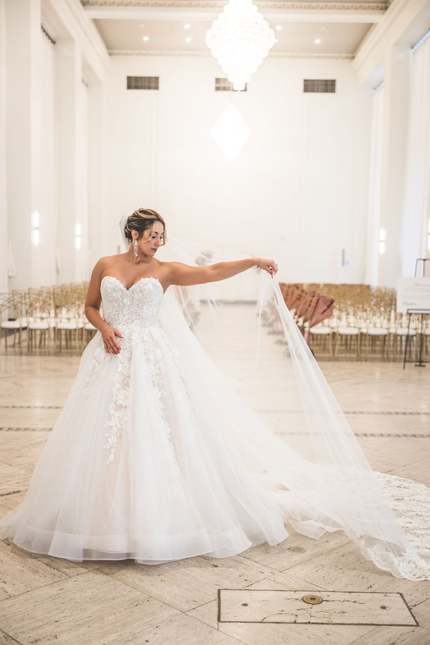 Bride in luxurious white gown poses gracefully while dancing in bright ballroom.