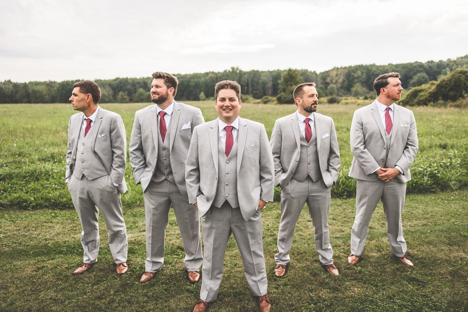 Groomsmen in light grey suits striking a pose in a green field.