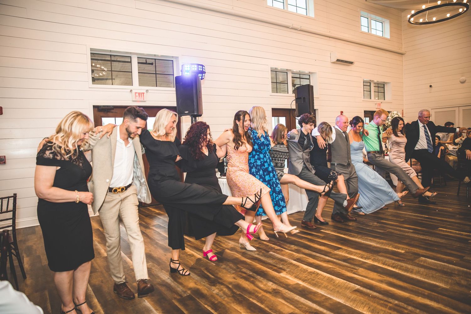 Wedding guests dancing in line formation on wooden dance floor with purple lighting.