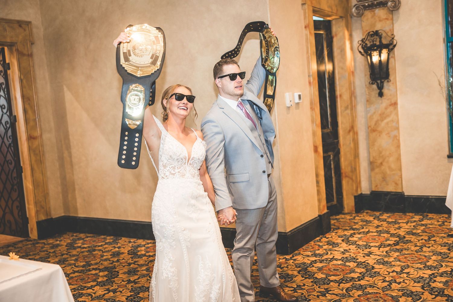 Wedding couple wearing sunglasses pose casually in an ornate indoor venue.
