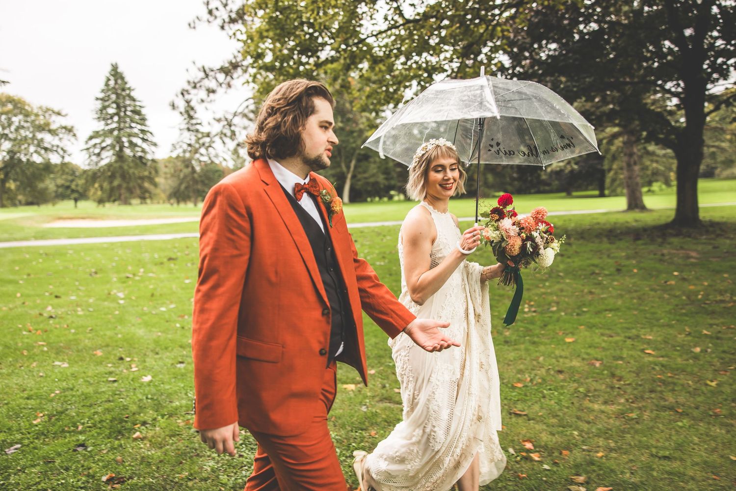 Joyful couple shares a laugh while walking with umbrella during autumn wedding.