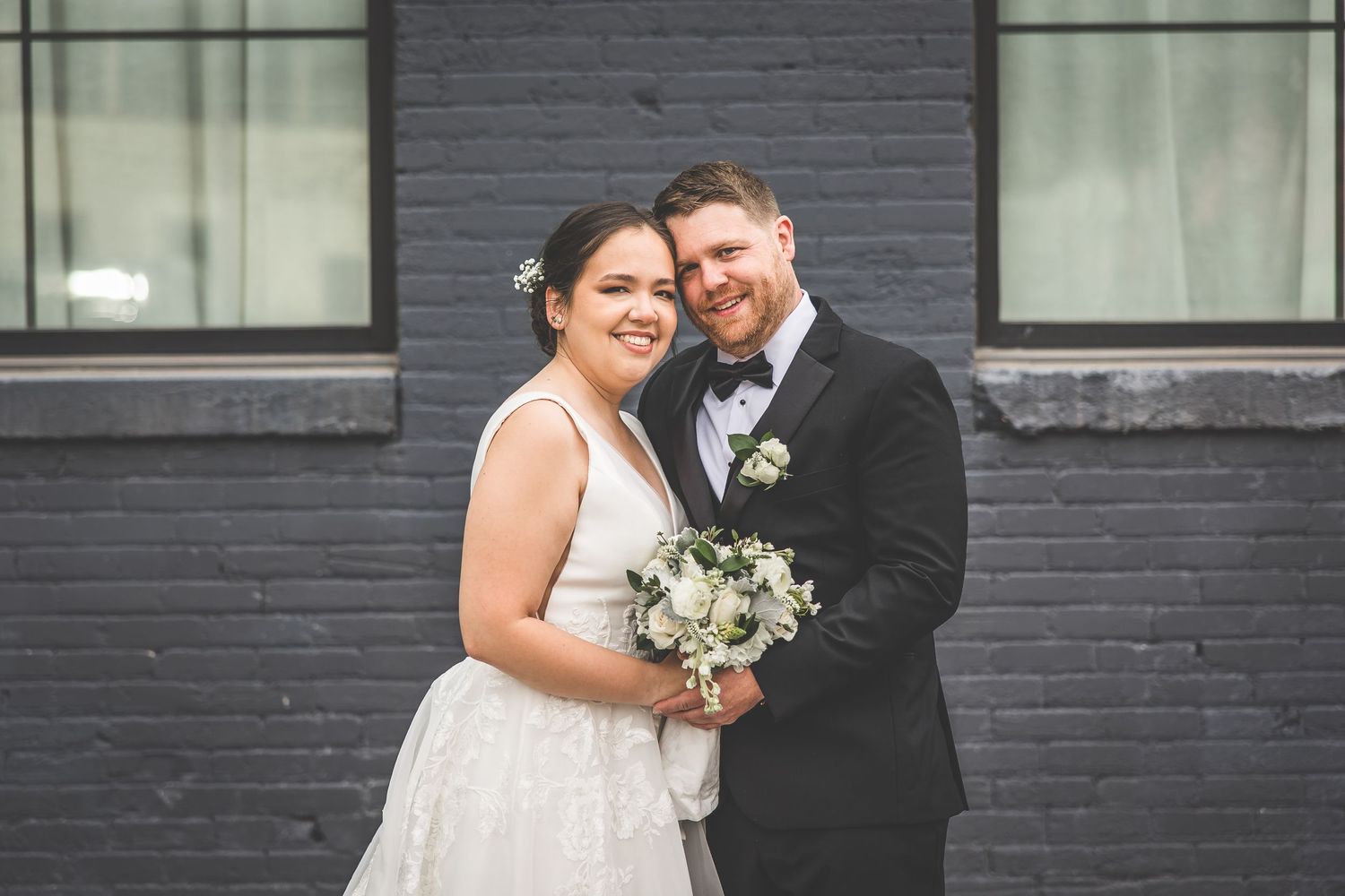 Newlyweds share an intimate moment in front of a modern building with large windows.