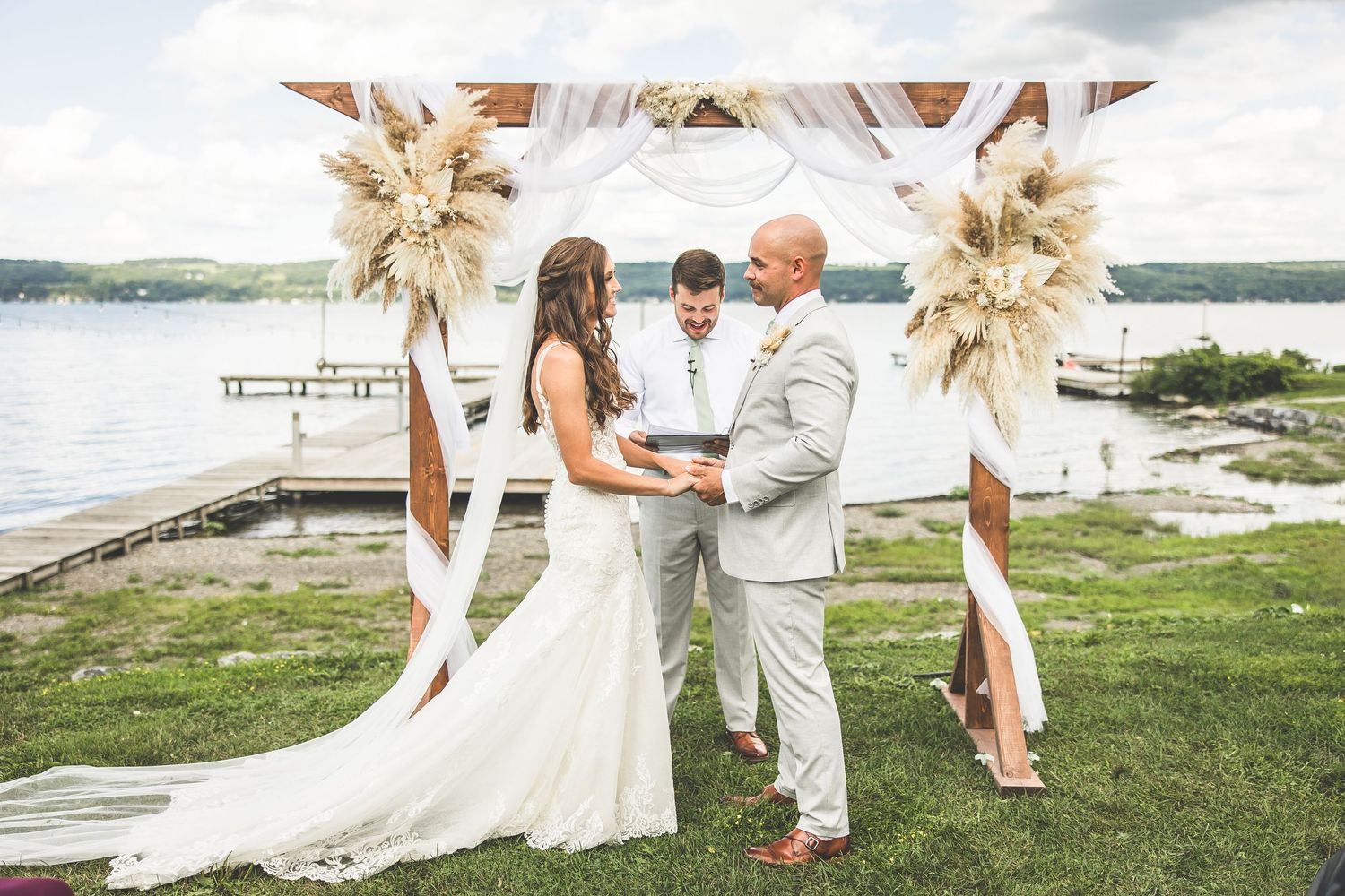 Outdoor waterfront wedding ceremony with dried pampas grass decorations and natural scenery.