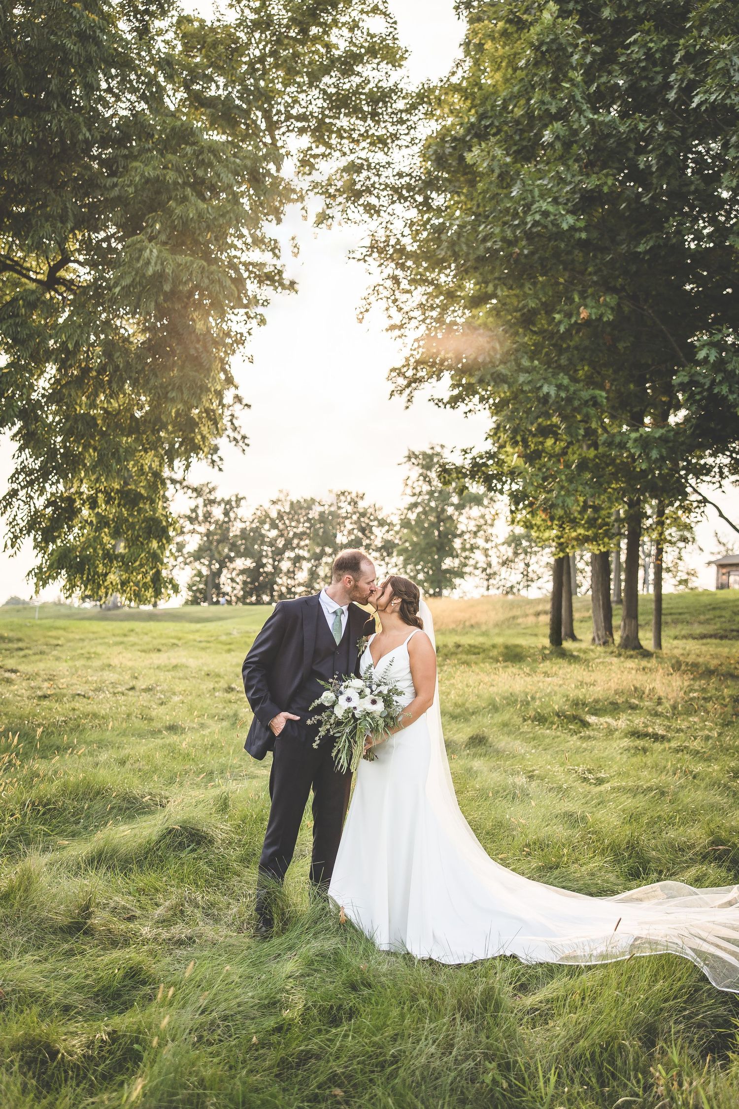 Couple shares intimate moments in a grassy field during golden hour wedding photoshoot.
