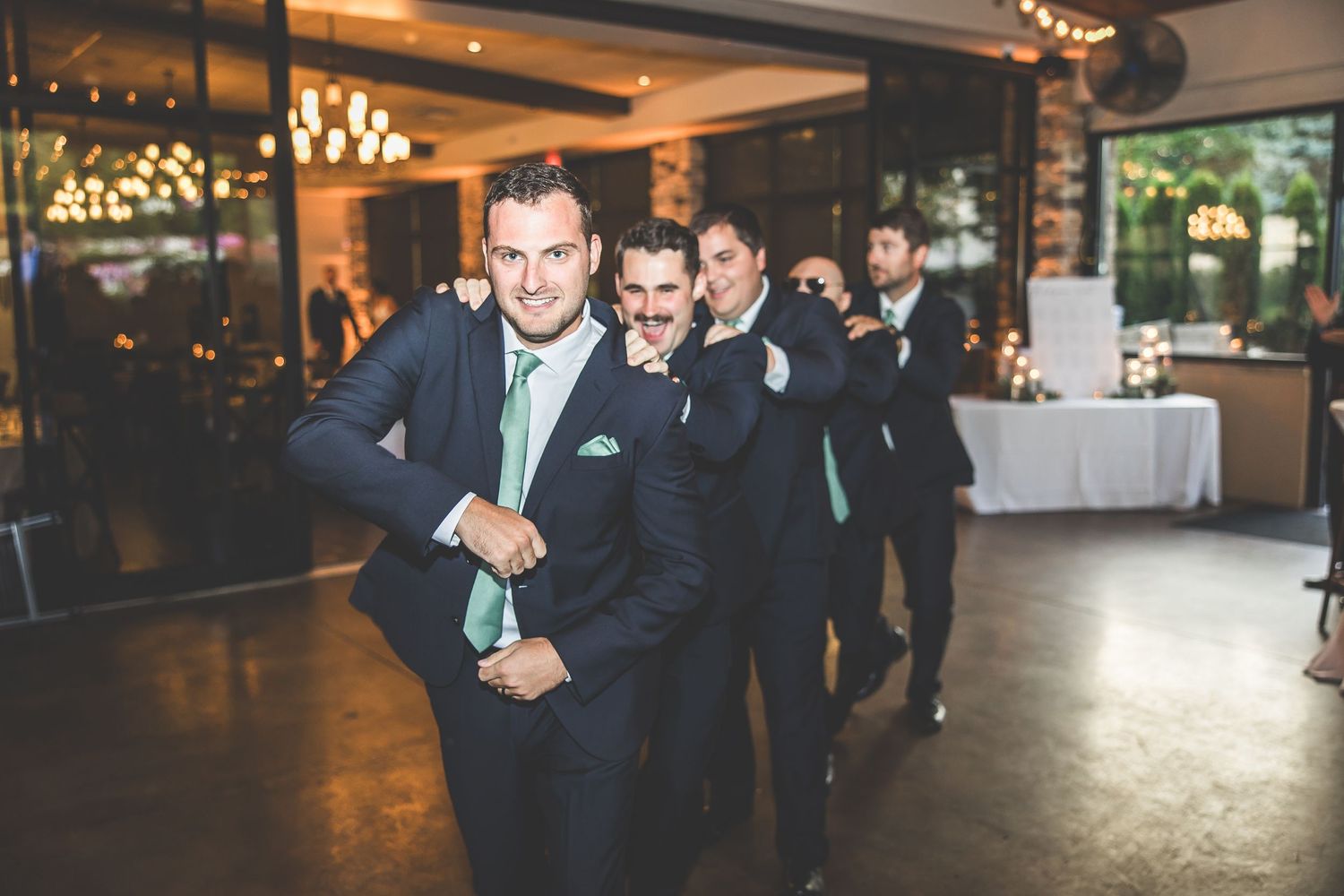 Groomsmen in dark suits making celebratory entrance at wedding reception venue.