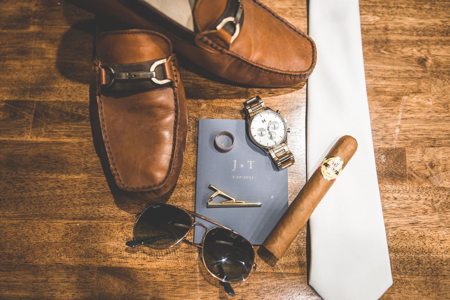 Brown leather shoes and accessories arranged on wooden surface.