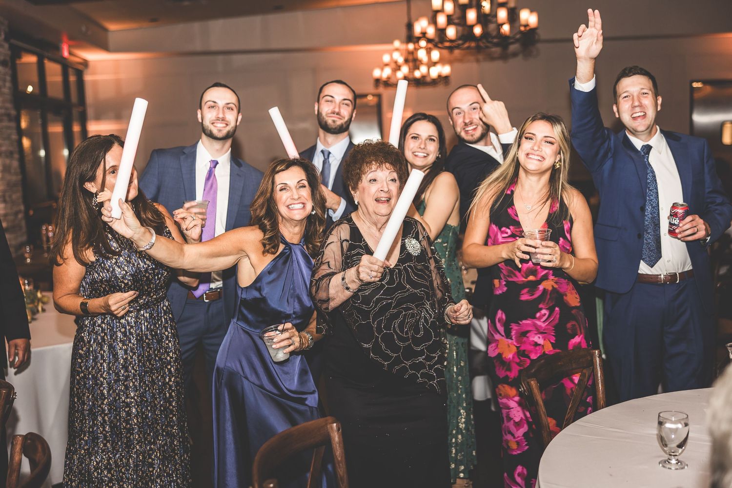 Group of wedding guests posing together under elegant chandelier lighting.